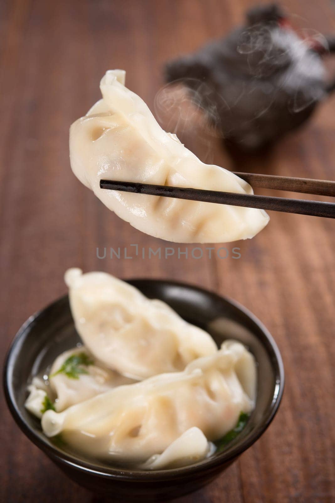 Fresh dumplings soup on plate with chopsticks and hot steams. Chinese food .on rustic old vintage wooden background.