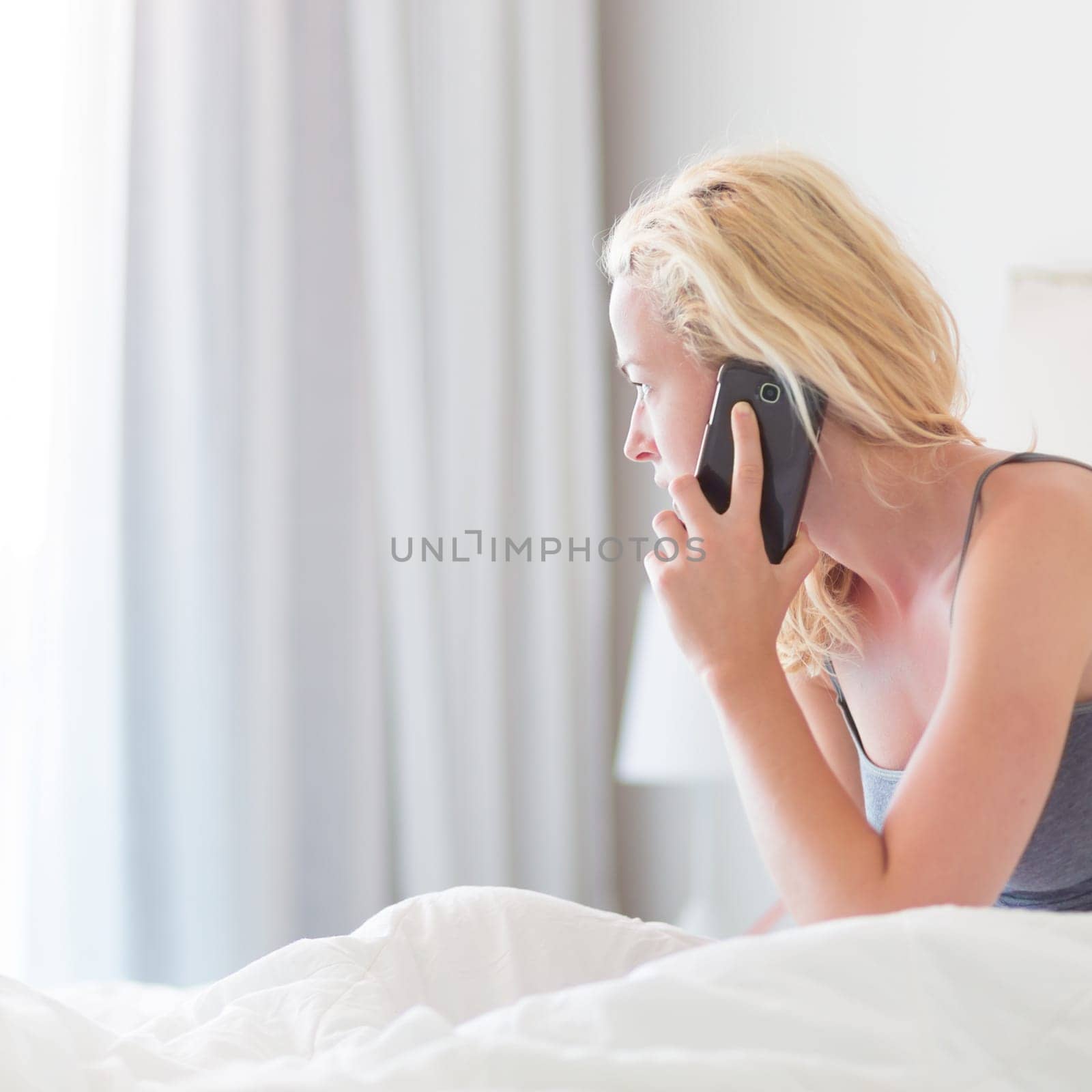 Portrait of  young lady with mobile phone in bed at home. Tired sleepy woman receiving emergency call in bed early in the morning.