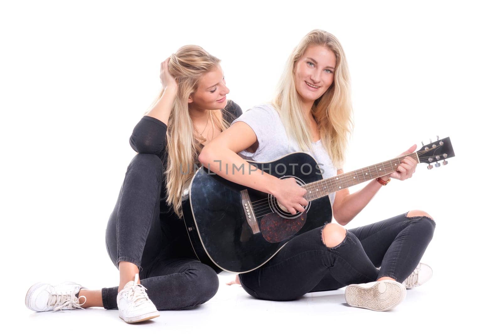 2 young girls sitting on the floor playing guitar