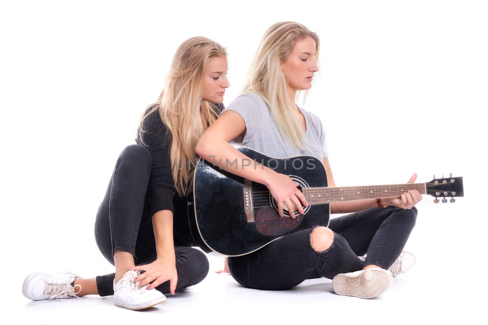 Blonde girl listens to her sister playing guitar
