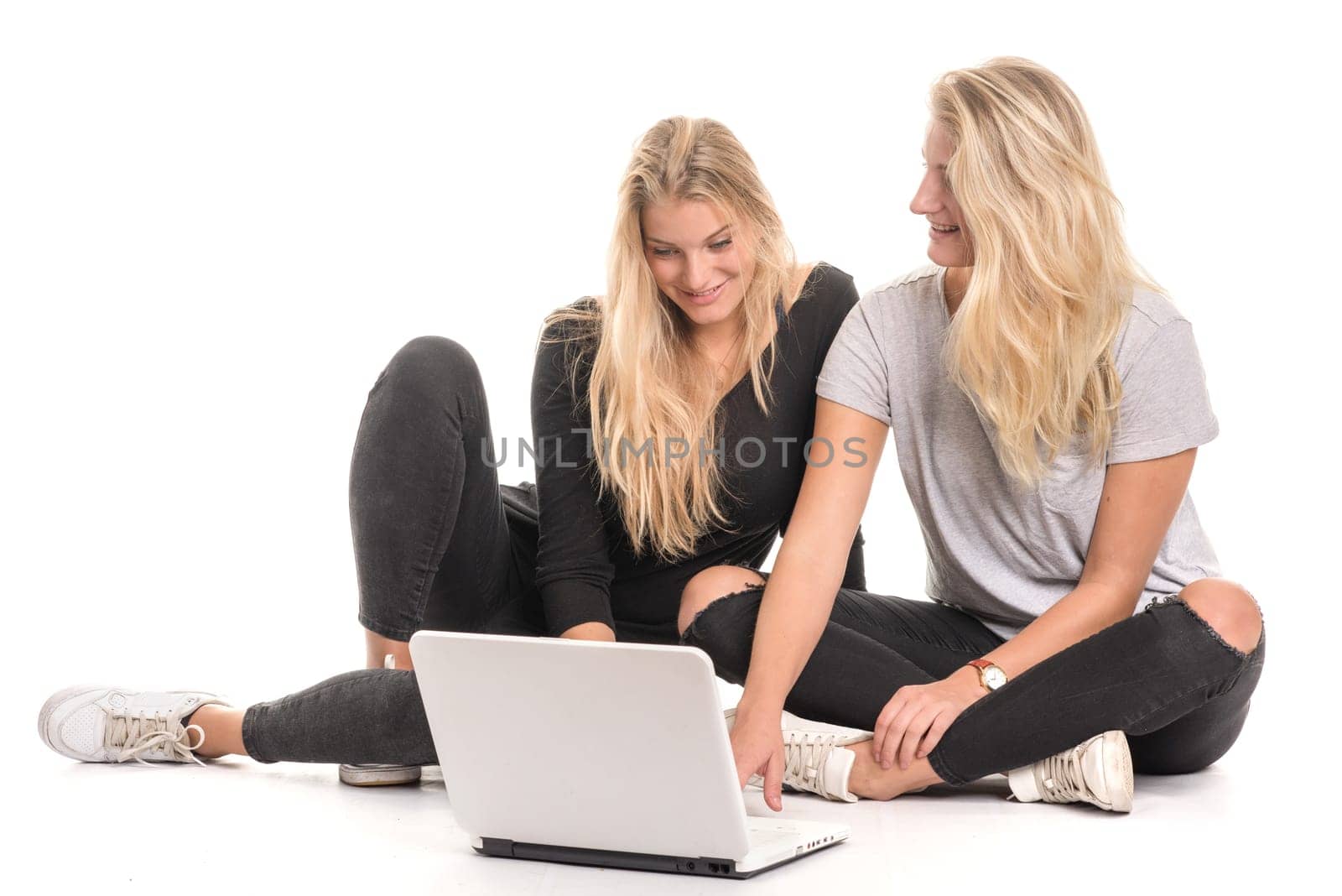 2 blonde girls sit on the floor and look into a laptop together