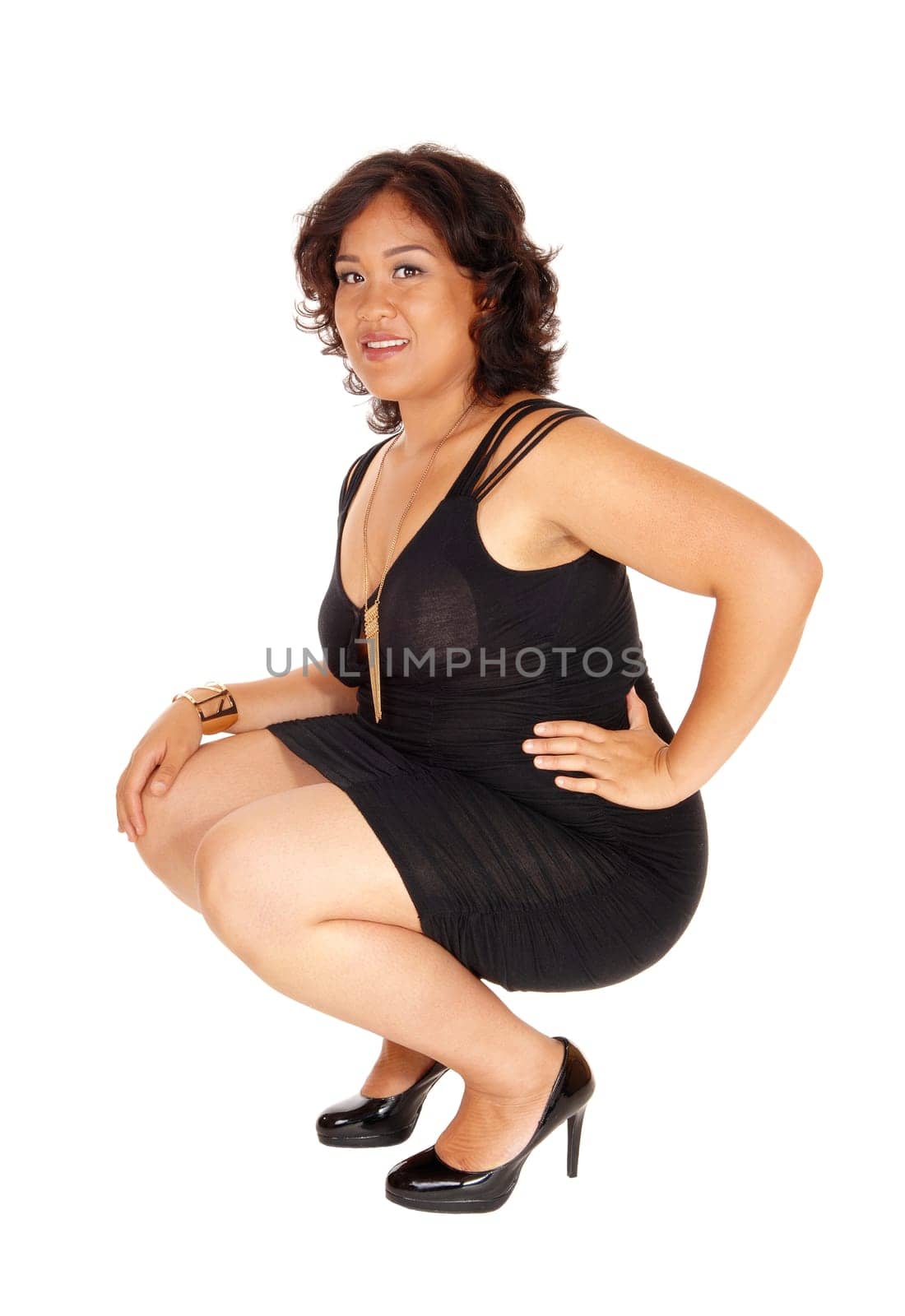 A young mixed raced woman in heels and black dress crouching on the .floor, isolated for white background..
