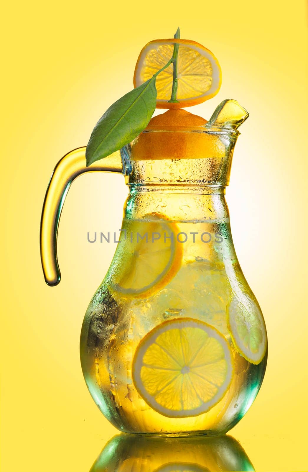 Misted lemonade pitcher with lemon slices and ice cubes decorated with quarter lemon cap  on yellow