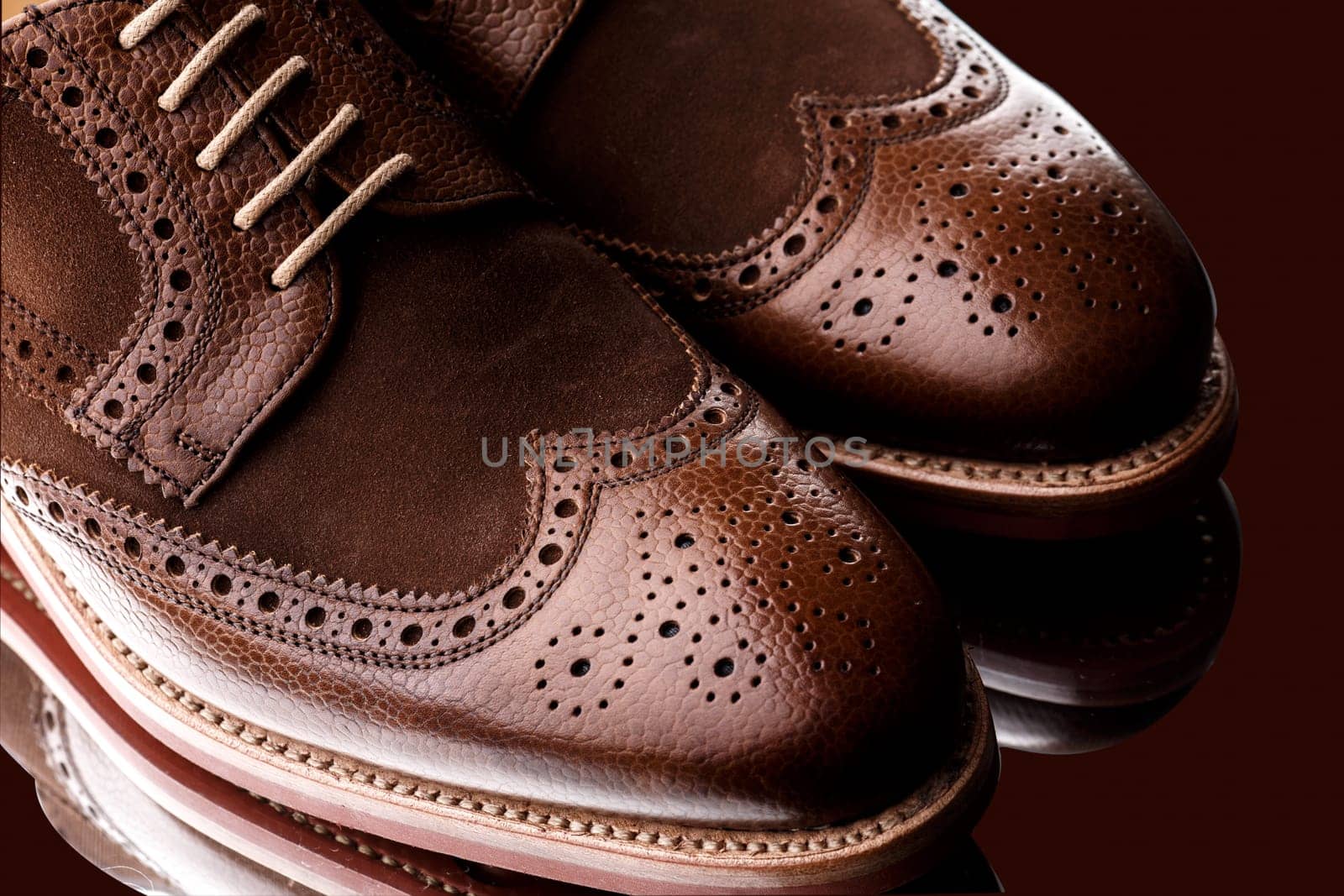 Unworn, laced pair of two tone men brogues (derbys) with elegant toe shape. The upper is stunning combination of brown calf with brown suede. Isolated on dark brown background with mirror reflection.