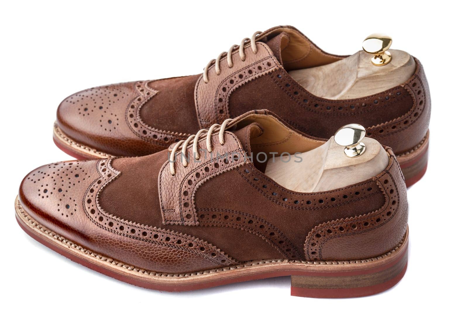 Unworn, laced pair of handcrafted shiny, two tone men brogues (also known as derbys, gibsons or wingtips) with shoe trees inserted on durable welted red brick rubber sole. The upper is stunning combination of brown calf with brown suede. Isolated on white background.