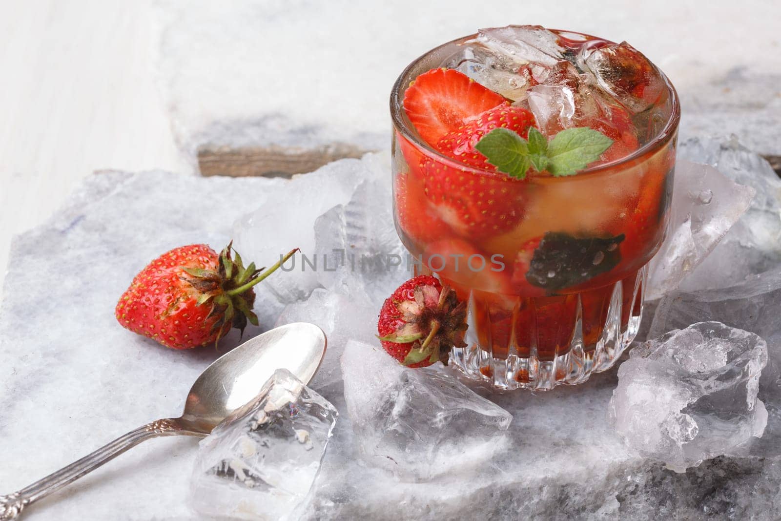 Strawberry mint bourbon smash served on a marble plate with crushed ice . Alcoholic cocktail with strawberry.
