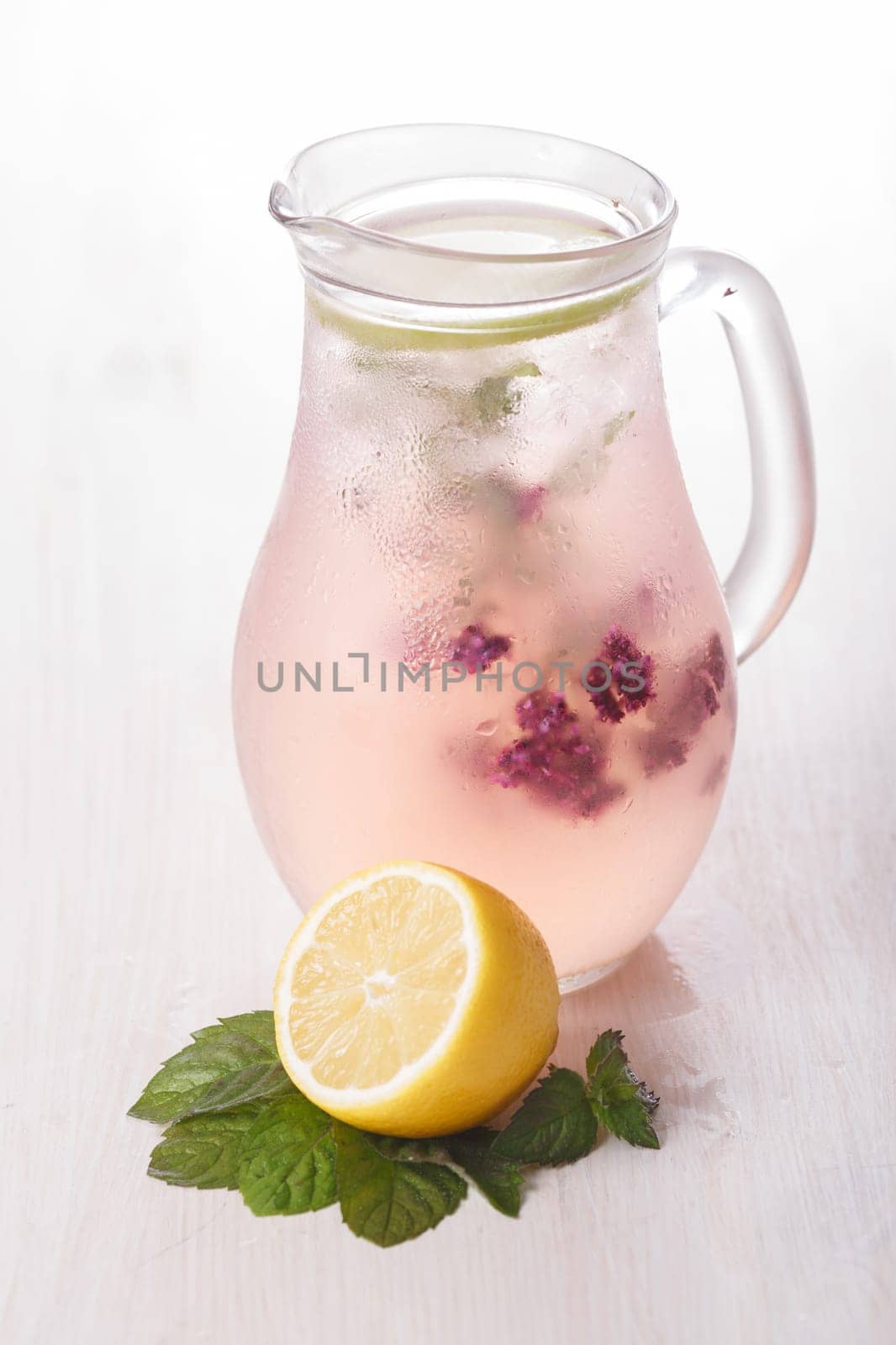 Blossoming oregano infused water. Pitcher of iced detox wated with wild marjoram (oregano) on a bleached wooden table. Clean eating concept