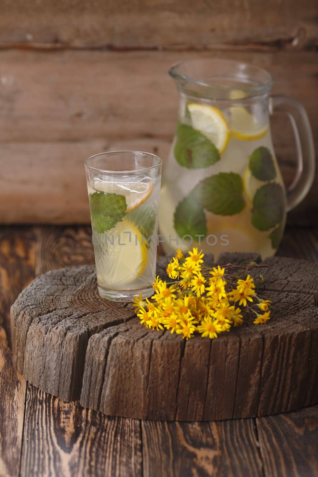 Pitcher of mint lemonade on a wooden table near yellow wild flowers