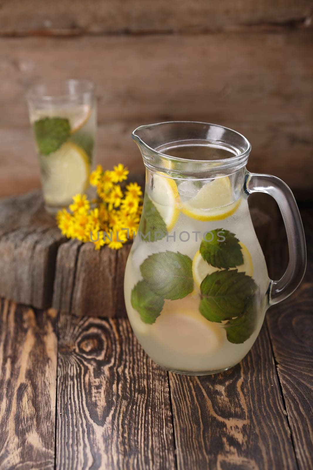 Pitcher of mint lemonade on a wooden table near yellow wild flowers