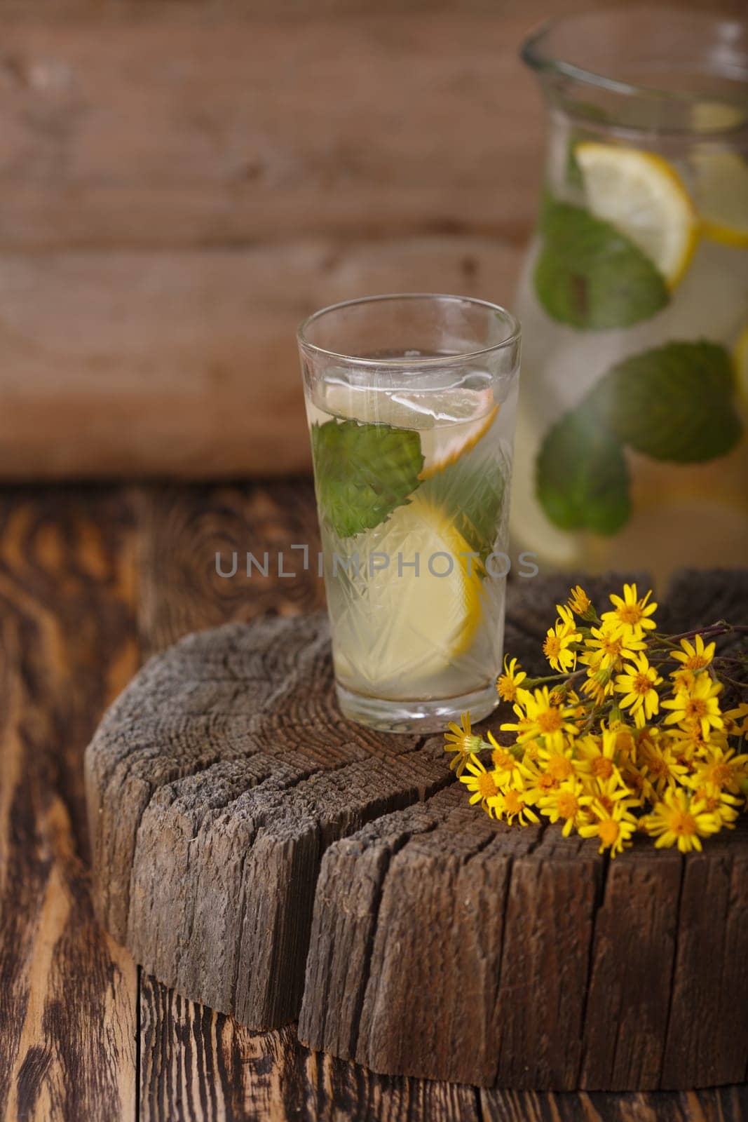 Pitcher of mint lemonade on a wooden table near yellow wild flowers