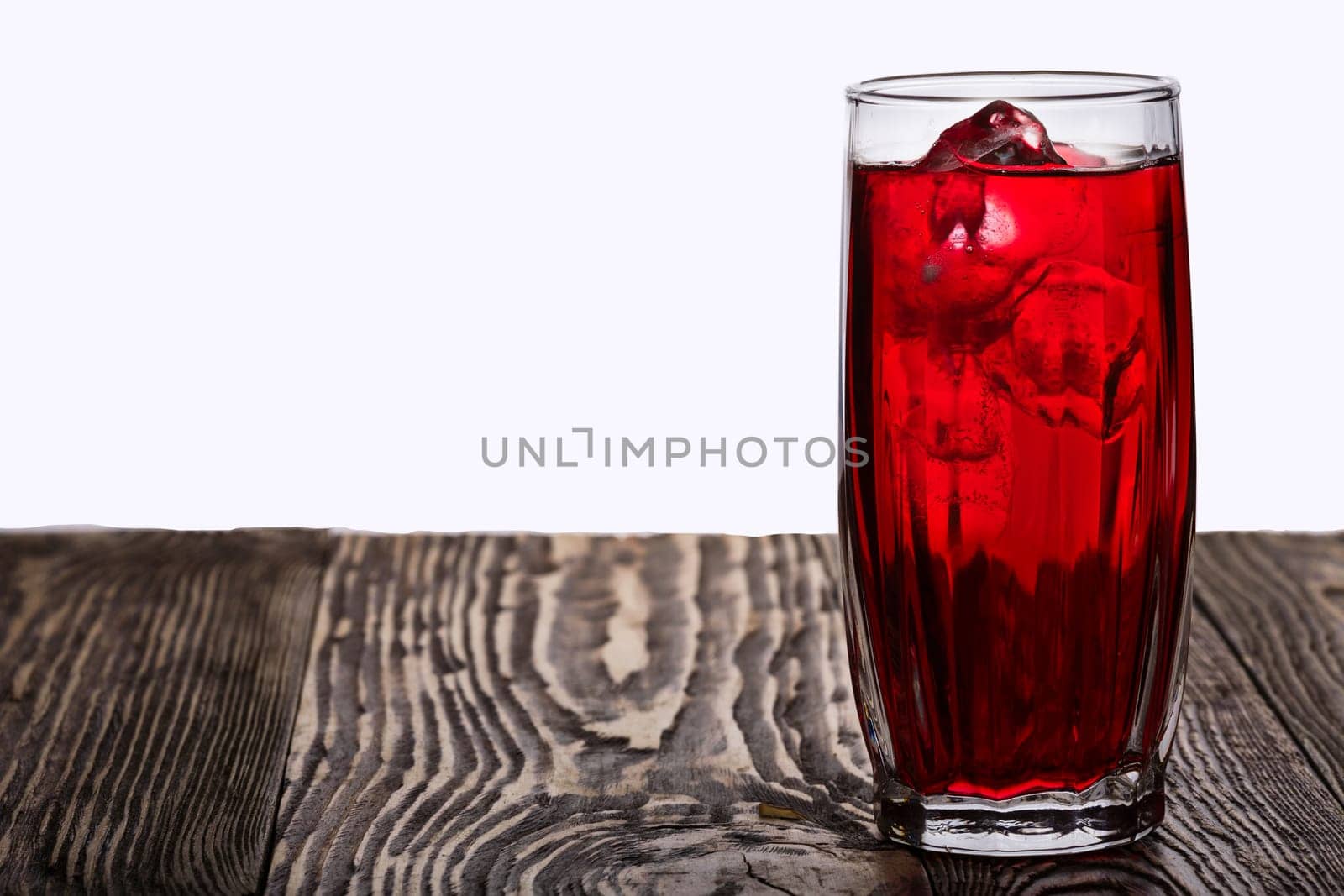 Iced hibiscus tea also known as Flor de Jamaica on wooden table  against plain background