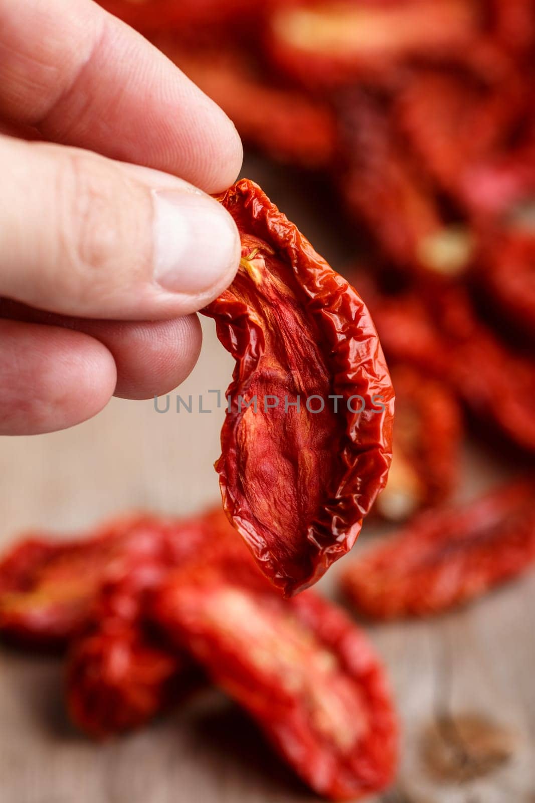 Male hand holding sun dried tomato against  dried tomatoes on wooden table . Selective focus
