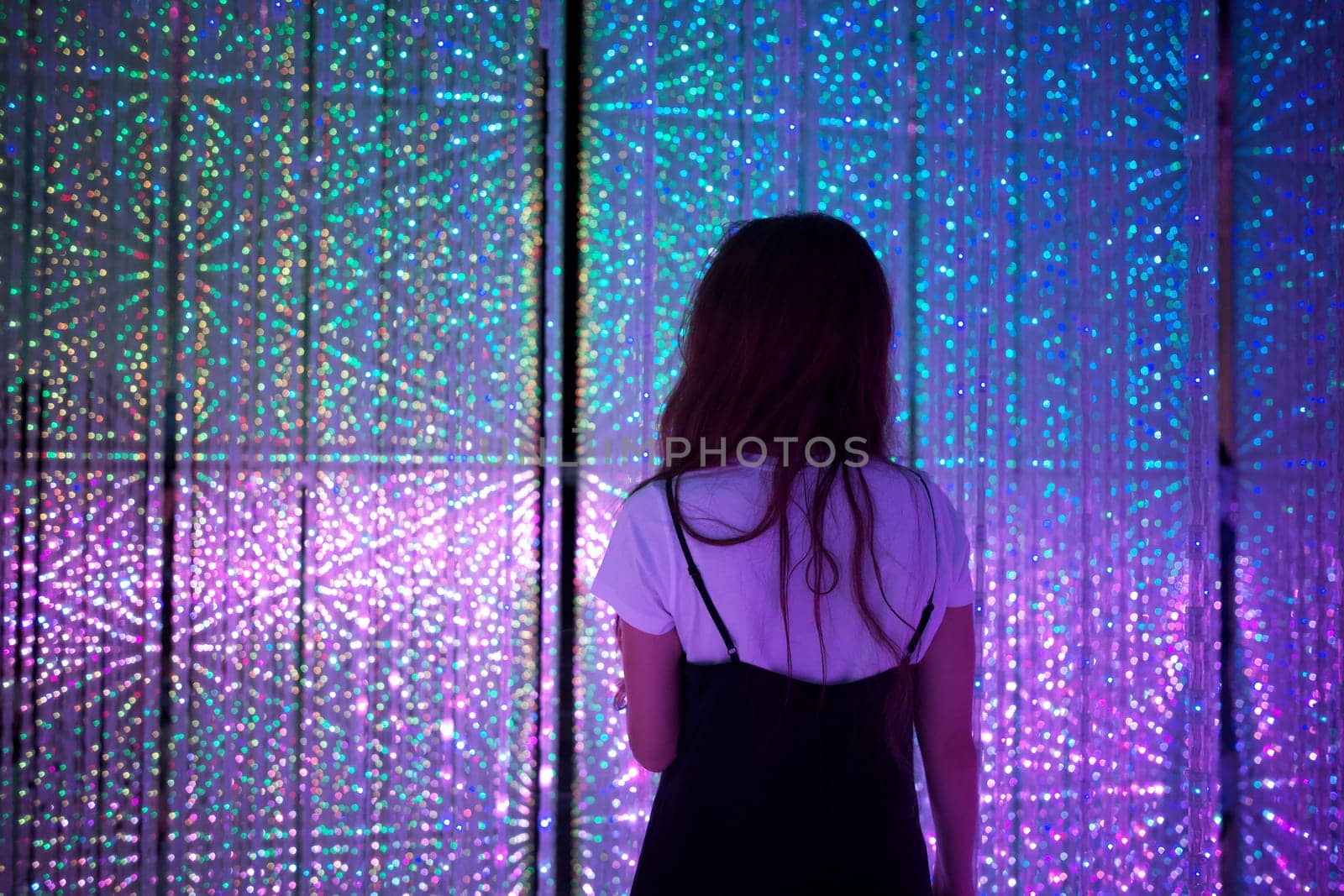 A woman standing amidst a dazzling light exhibit at TeamLab Tokyo, surrounded by vibrant colors and immersive digital art.