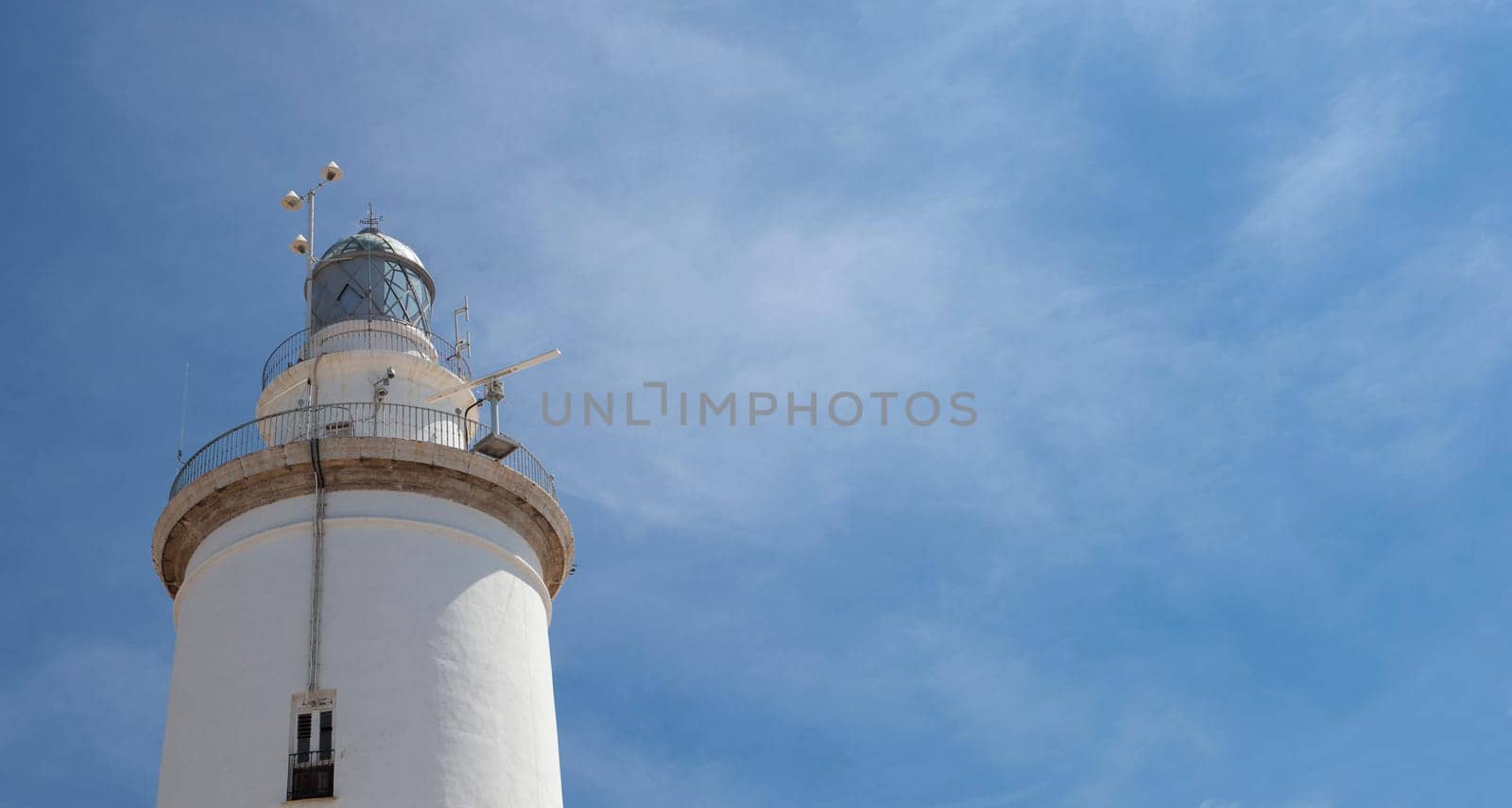 A white whitewashed lighthouse isolated over blue sky with clouds
