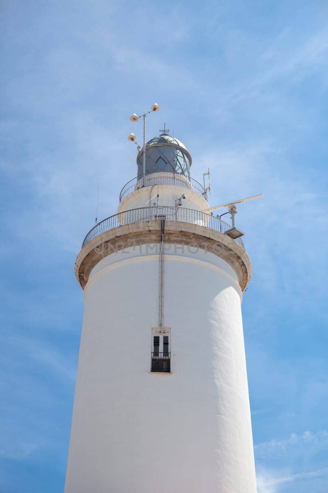 A white whitewashed lighthouse isolated over blue sky with clouds