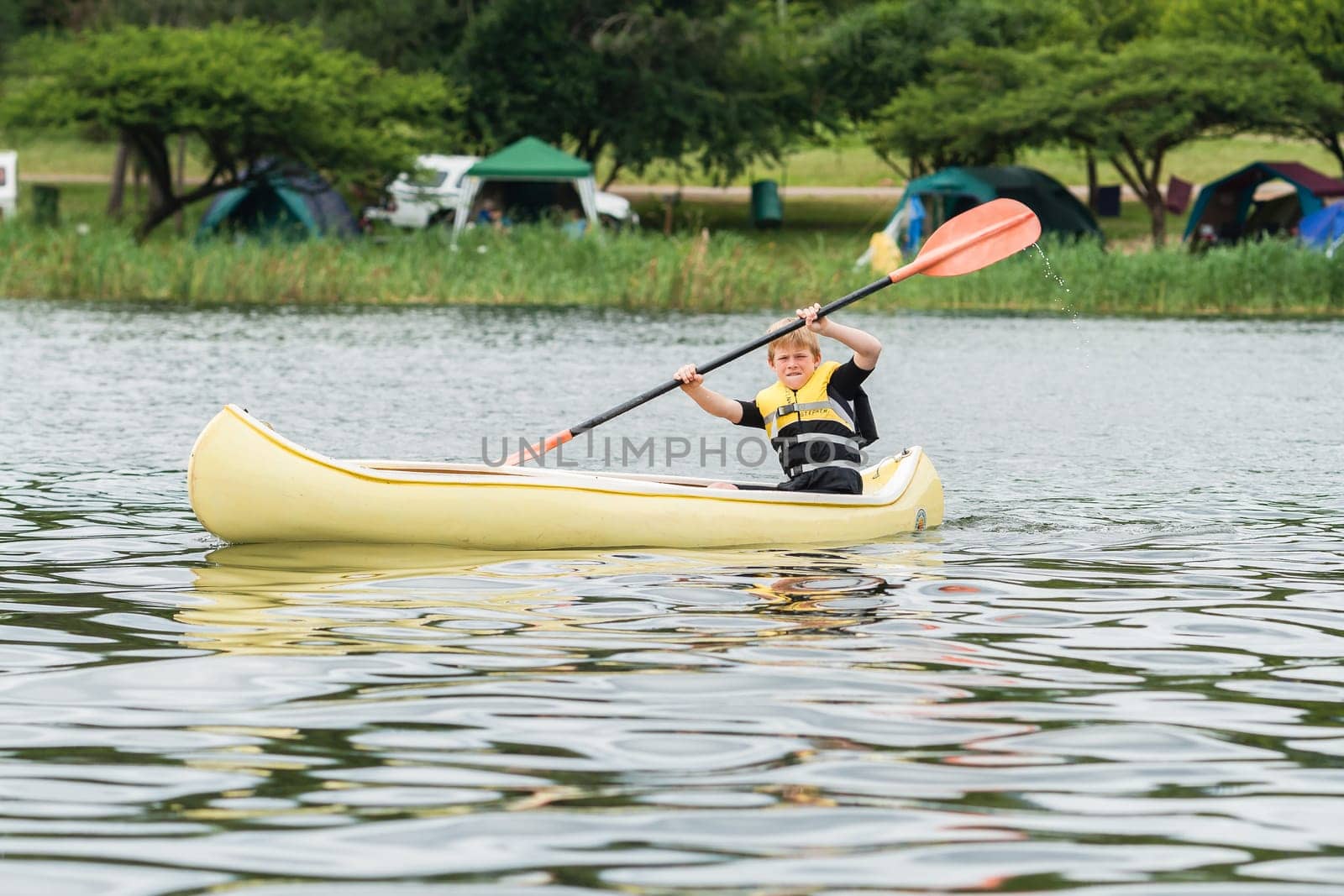 Young boy on holiday canoeing on dam waters
