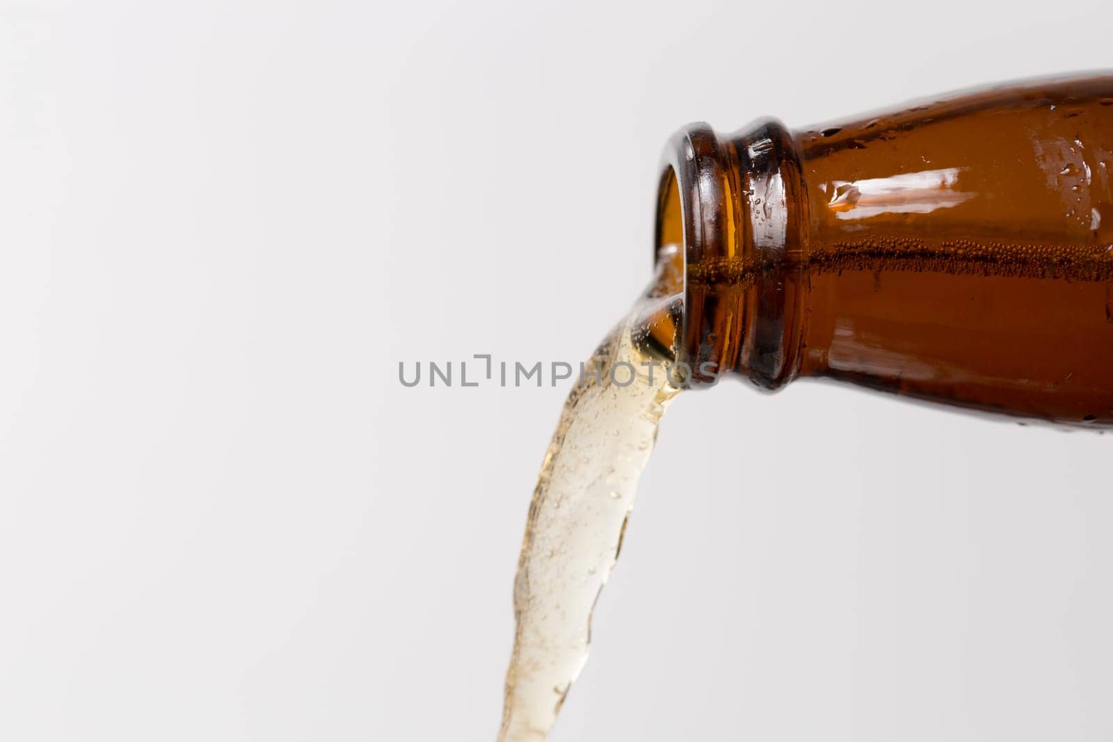 Beer Puring From Bottle with grey/white background with bubbles in the beer.
