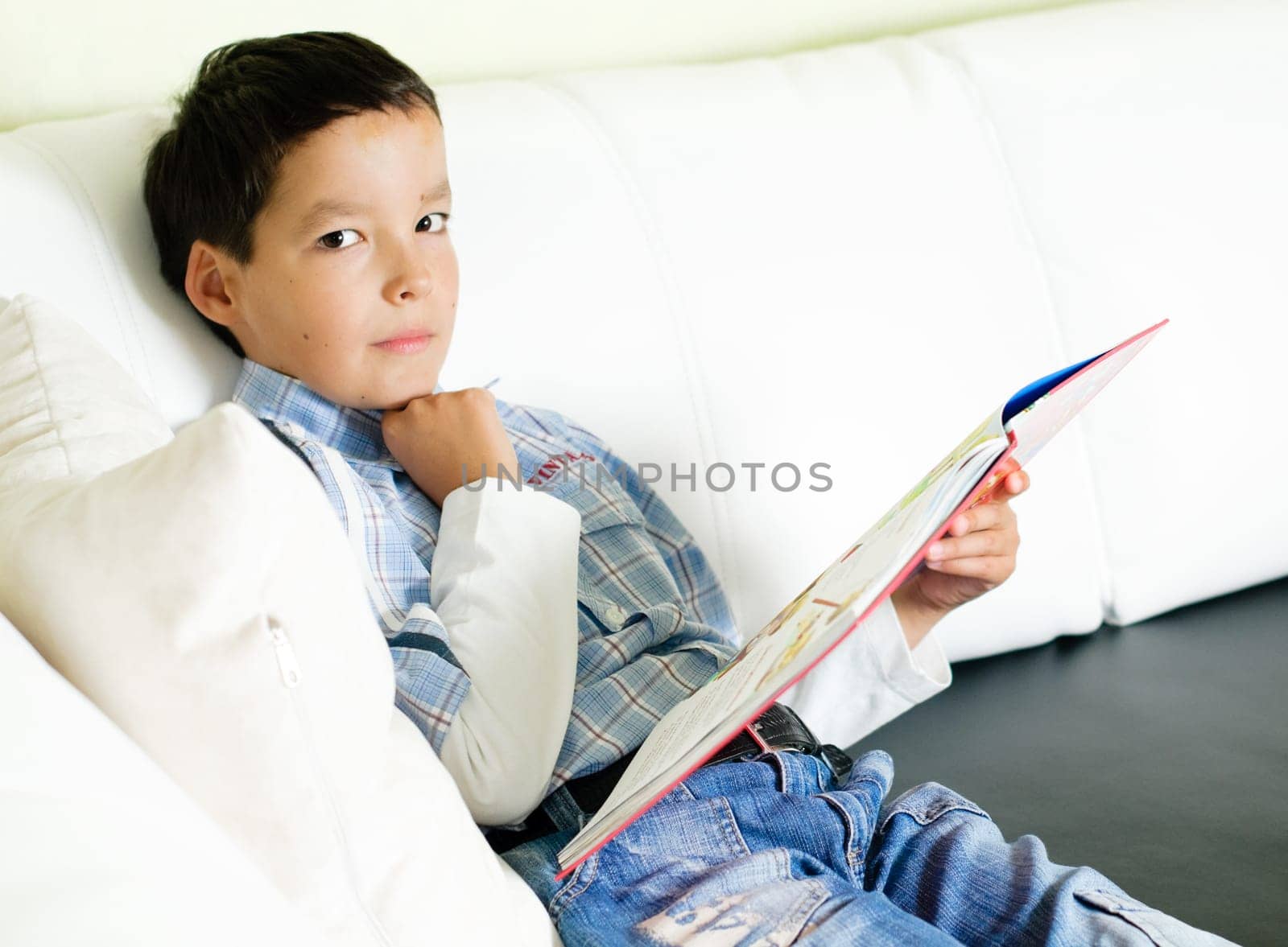 thoughtful little boy sitting on a sofa and reading a book