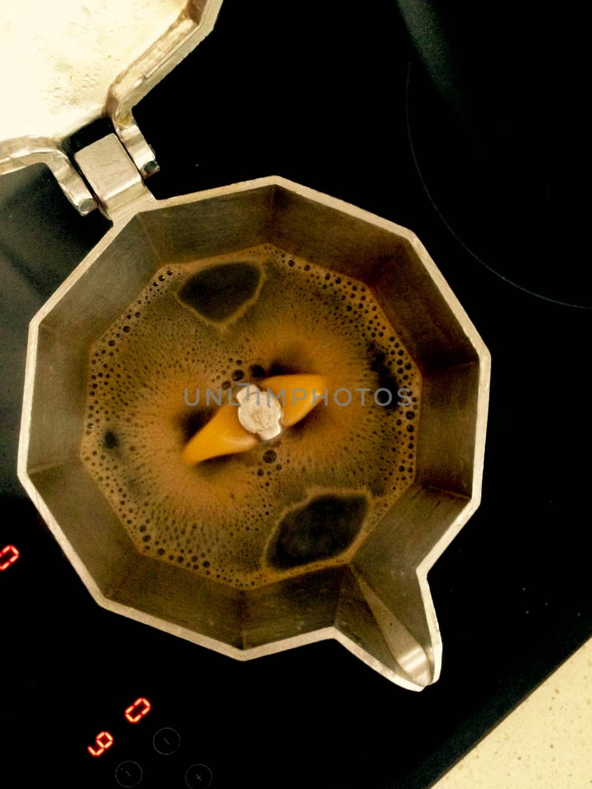 A metal coffeepot brewing Italian espresso coffee over glass-ceramic hob. High view