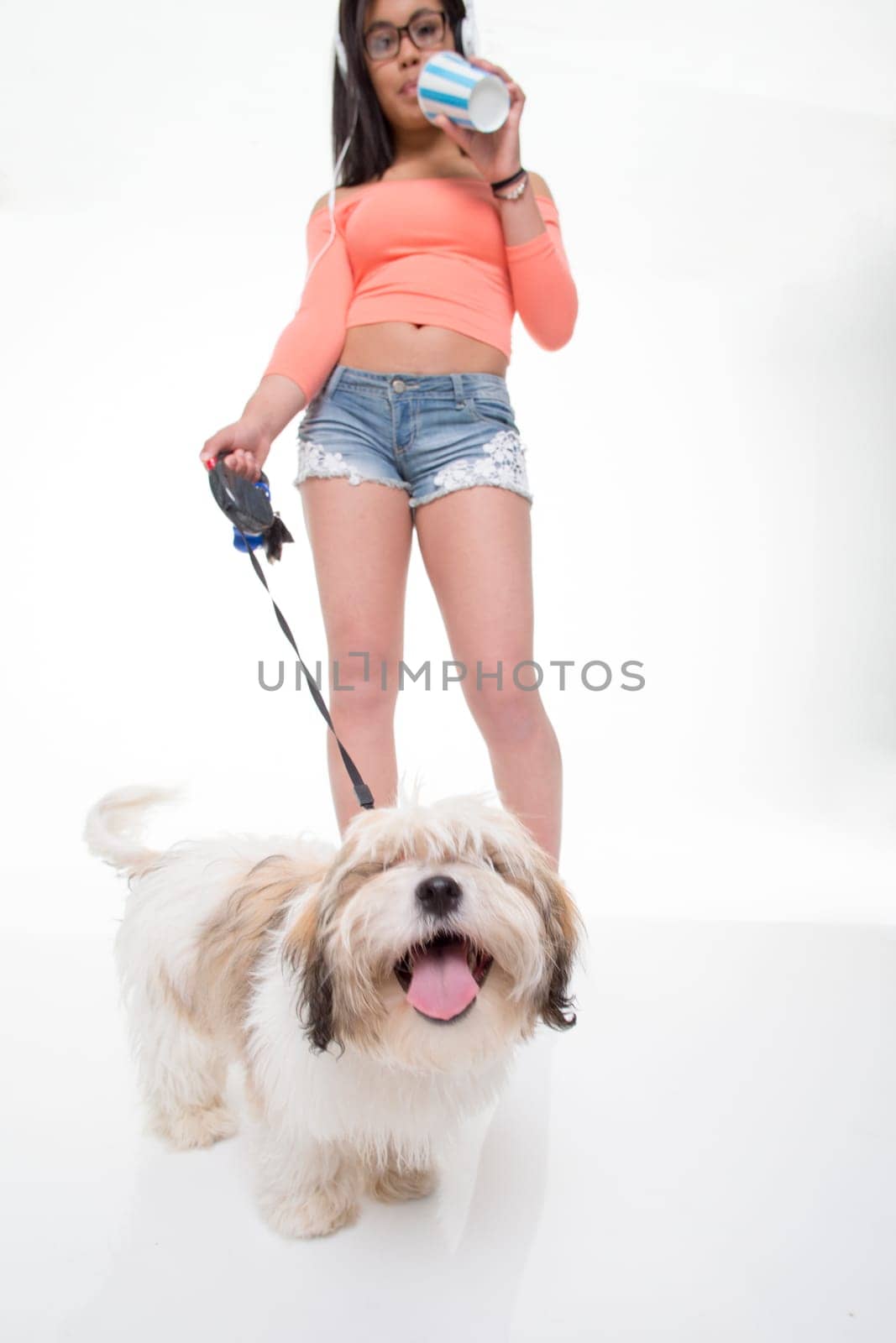 Portrait of a teenage girl with a dog on a leader on a white background. She is wearing summery clothing and has earphones in.