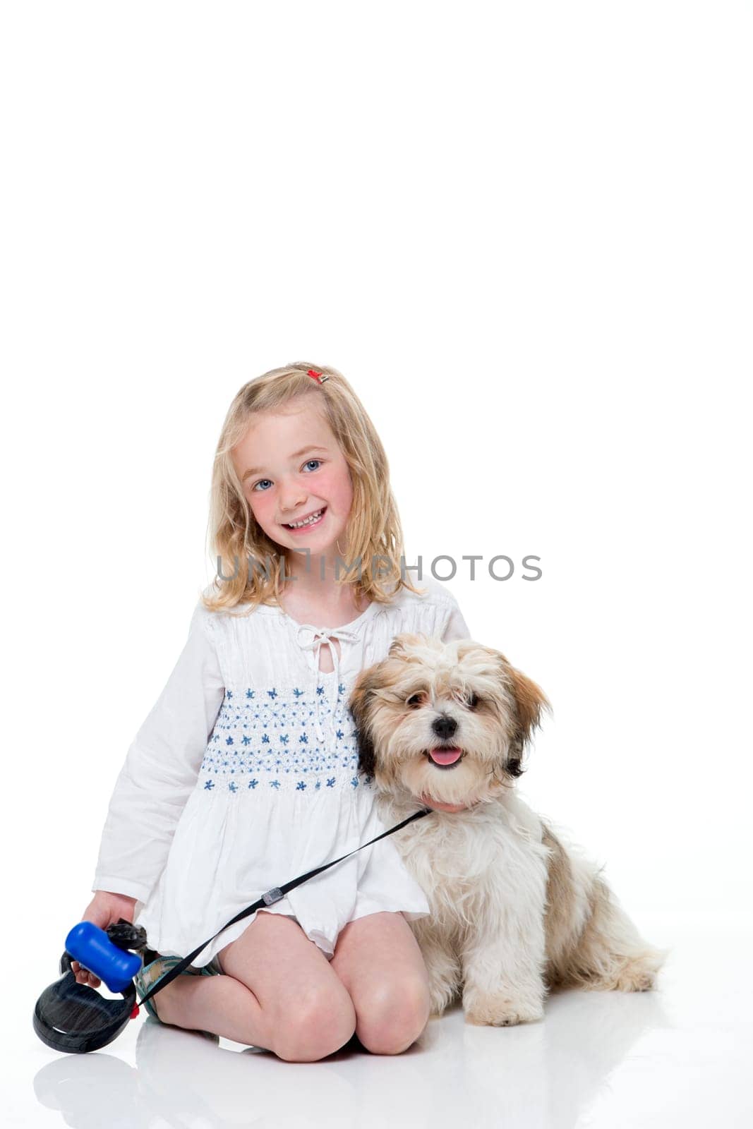 Portrait of a little girl sitting down with her dog. She is looking at the camera and smiling.