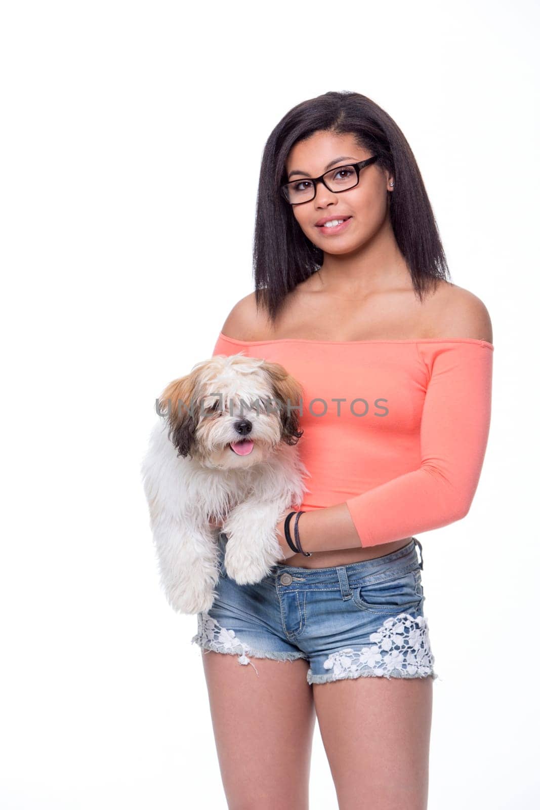 Teenage girl with her dog against a white background. She is wearing summery clothes and is looking at the camera.
