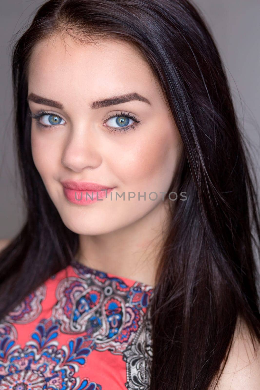 Portrait of a young woman taken in a studio. She is looking at the camera and smiling.