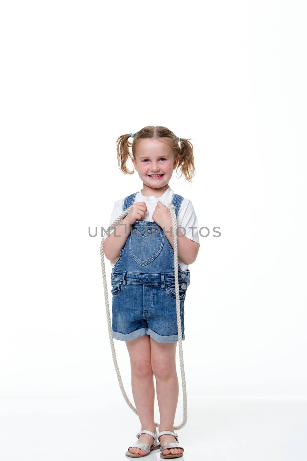 Portrait of a young girl skipping with a white background. She is wearing casual clothing and looking at the camera and smiling.