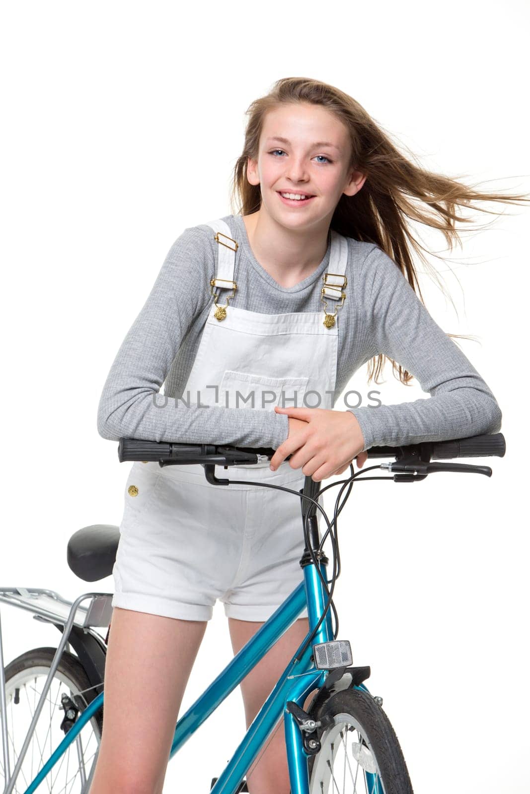 Young girl on a bicycle with a white background. She is smilng at the camera and wearing casual clothing.