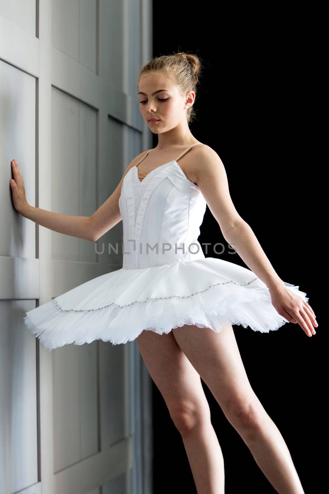 A young girl in a ballerina costume resting against the wall with a dark background.