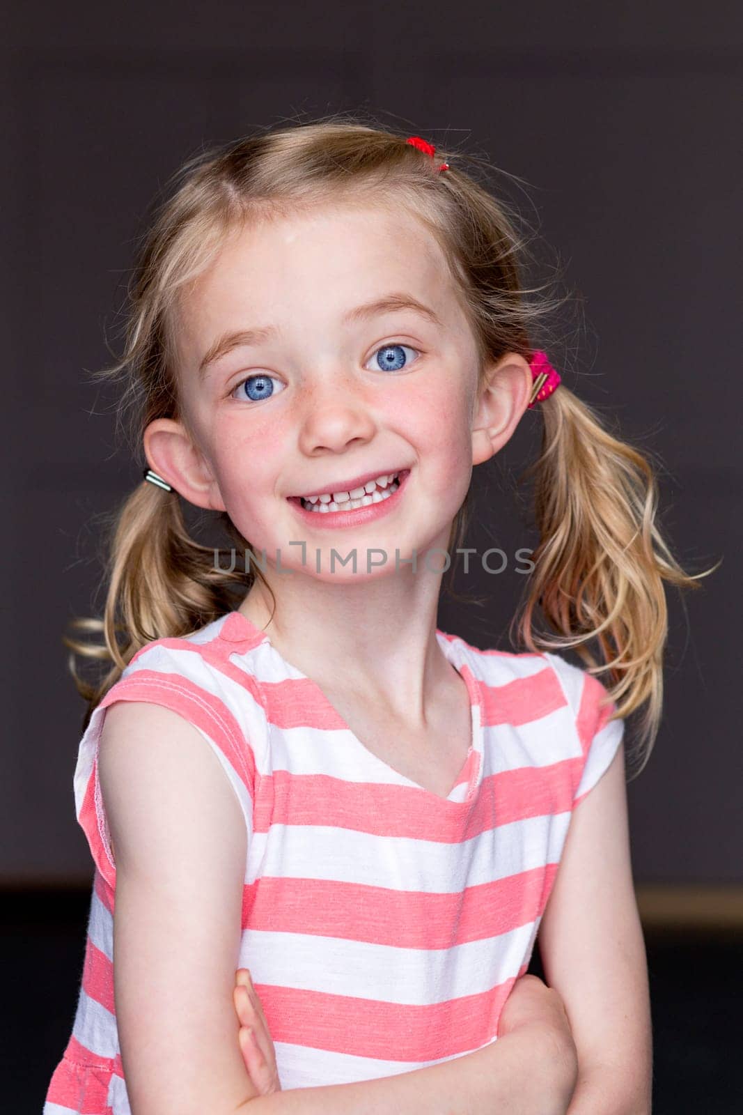 Portrait of a young girl with a grey background. She is smiling and looking at the camera.