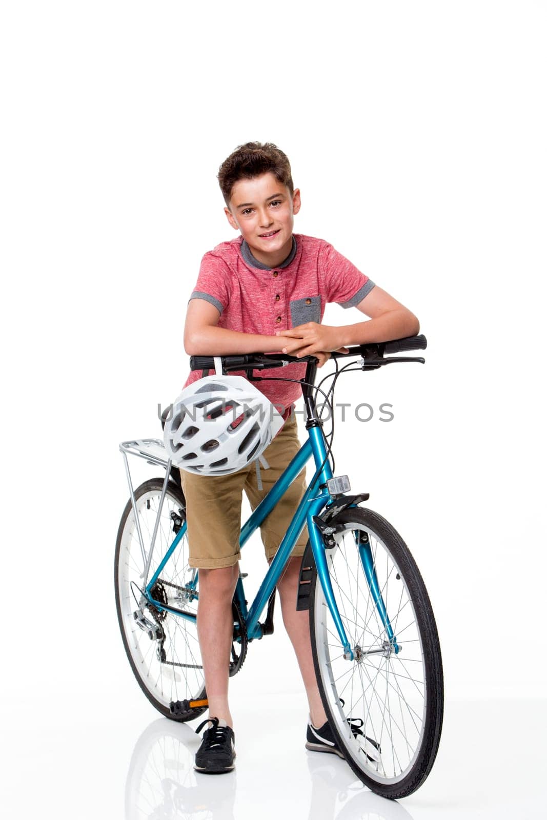 Young boy on a bike on a white background. He is wearing casual clothing and smiling at the camera.