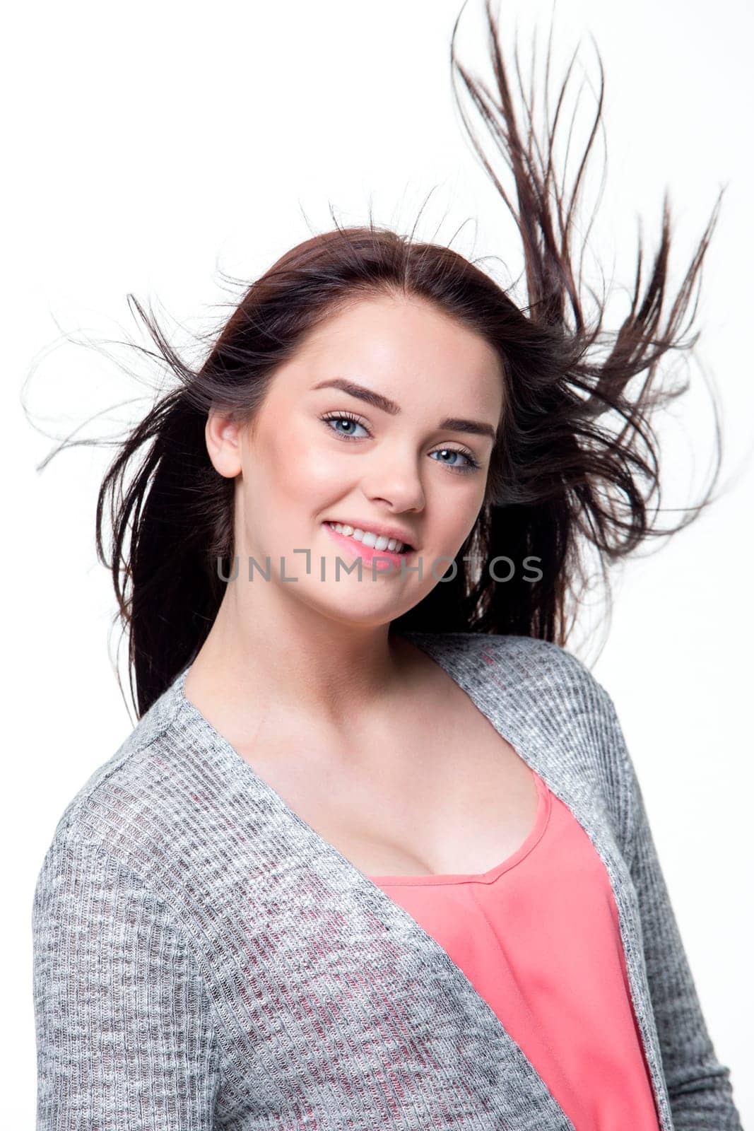 Portrait of a beautiful young woman with a white background. She is wearing casual clothing and looking at the camera and smiling.