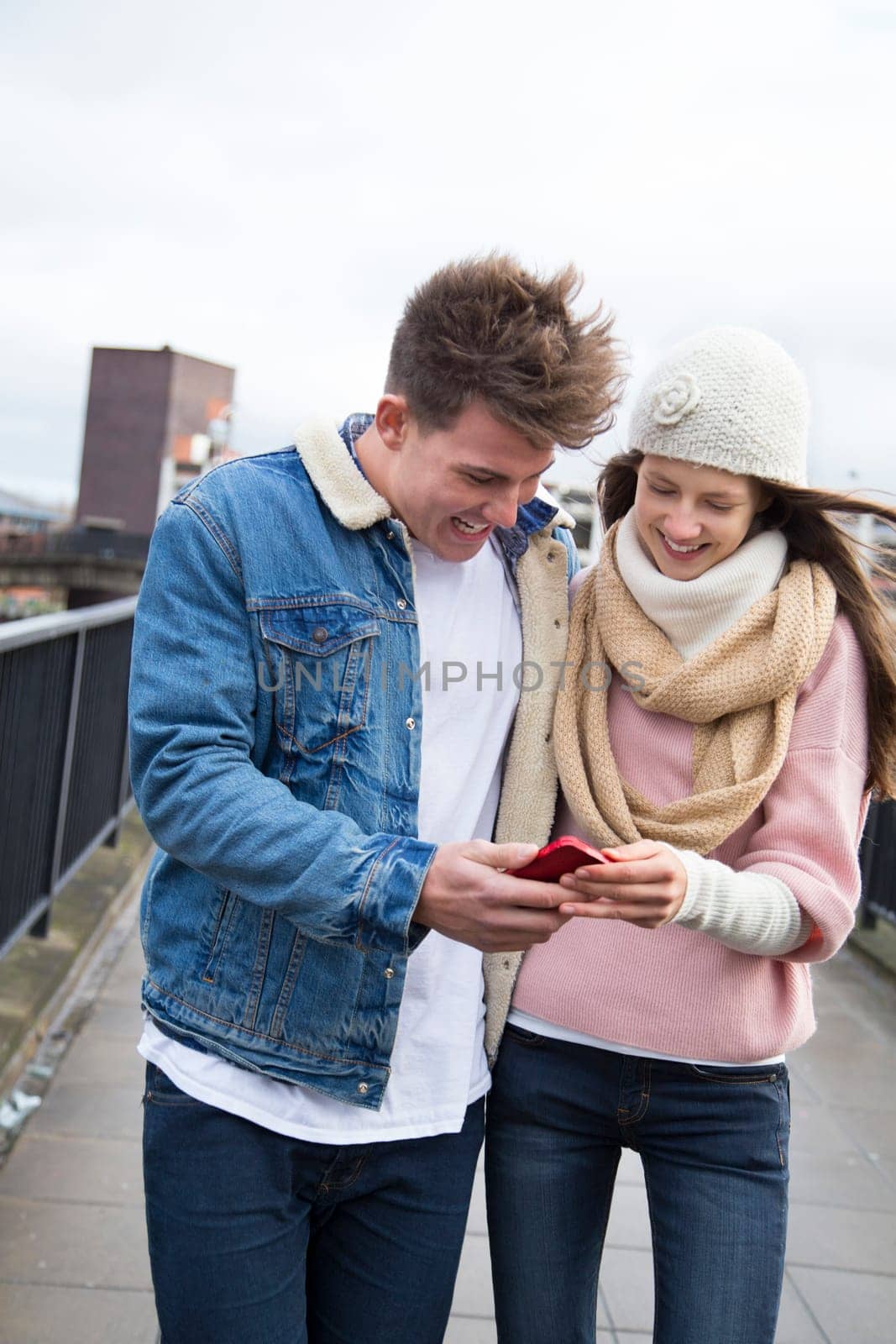 Young couple walking together in the cold weather, looking at a smartphone together.