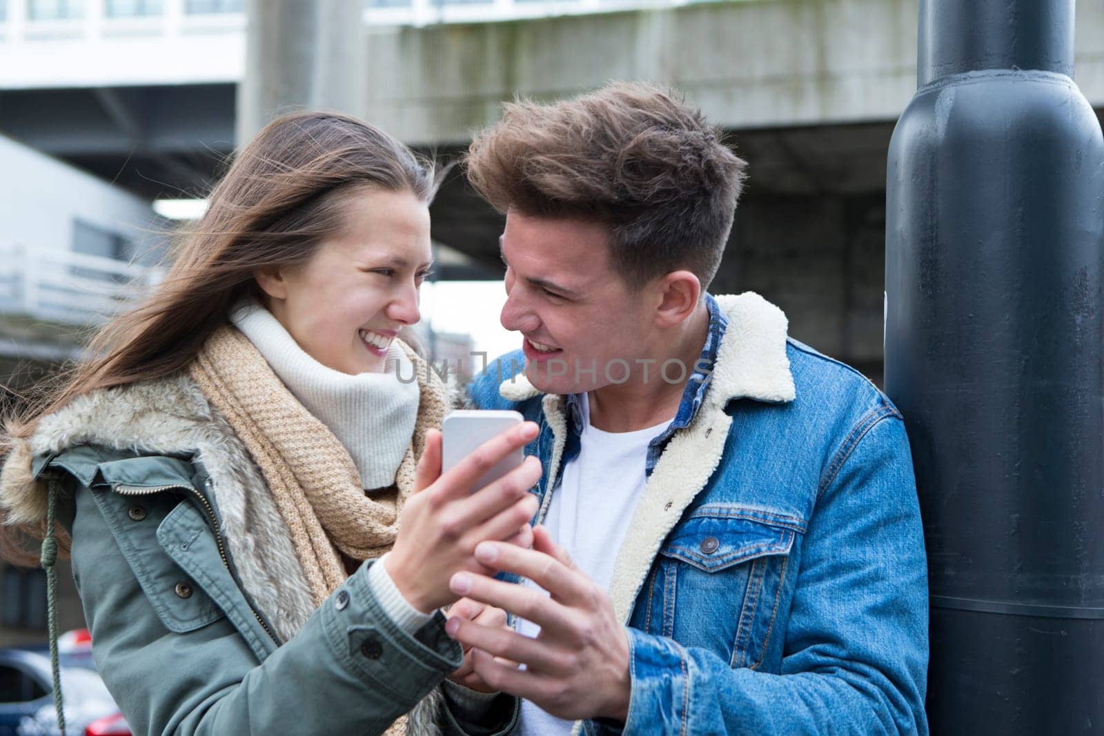 Young couple standing together in the cold weather, looking at a smartphone together