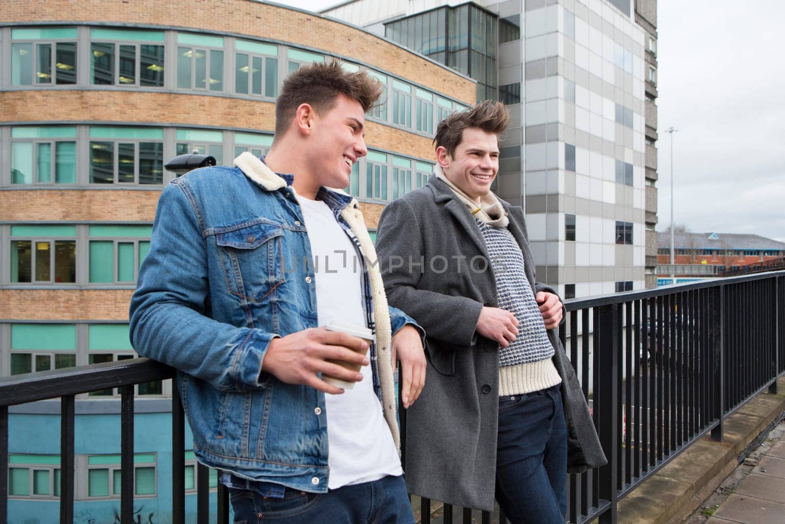Two young men talking in the city. One is holding a disposable coffee cup.
