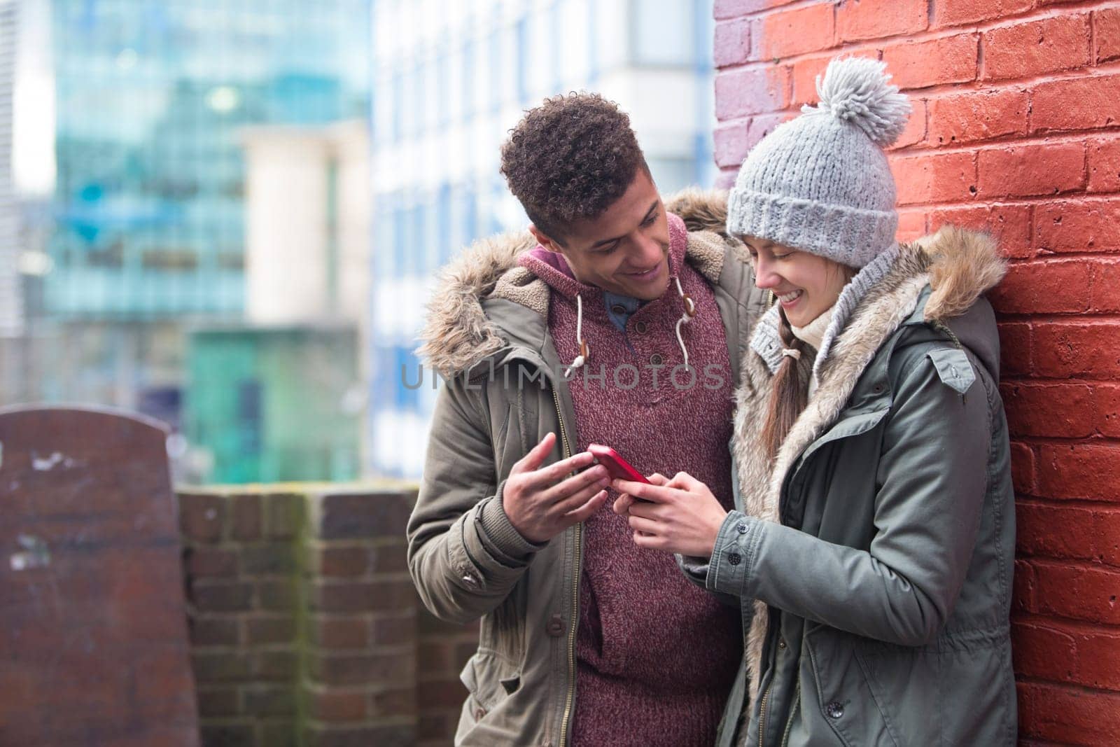 Young couple standing together in the cold weather, looking at a smartphone
