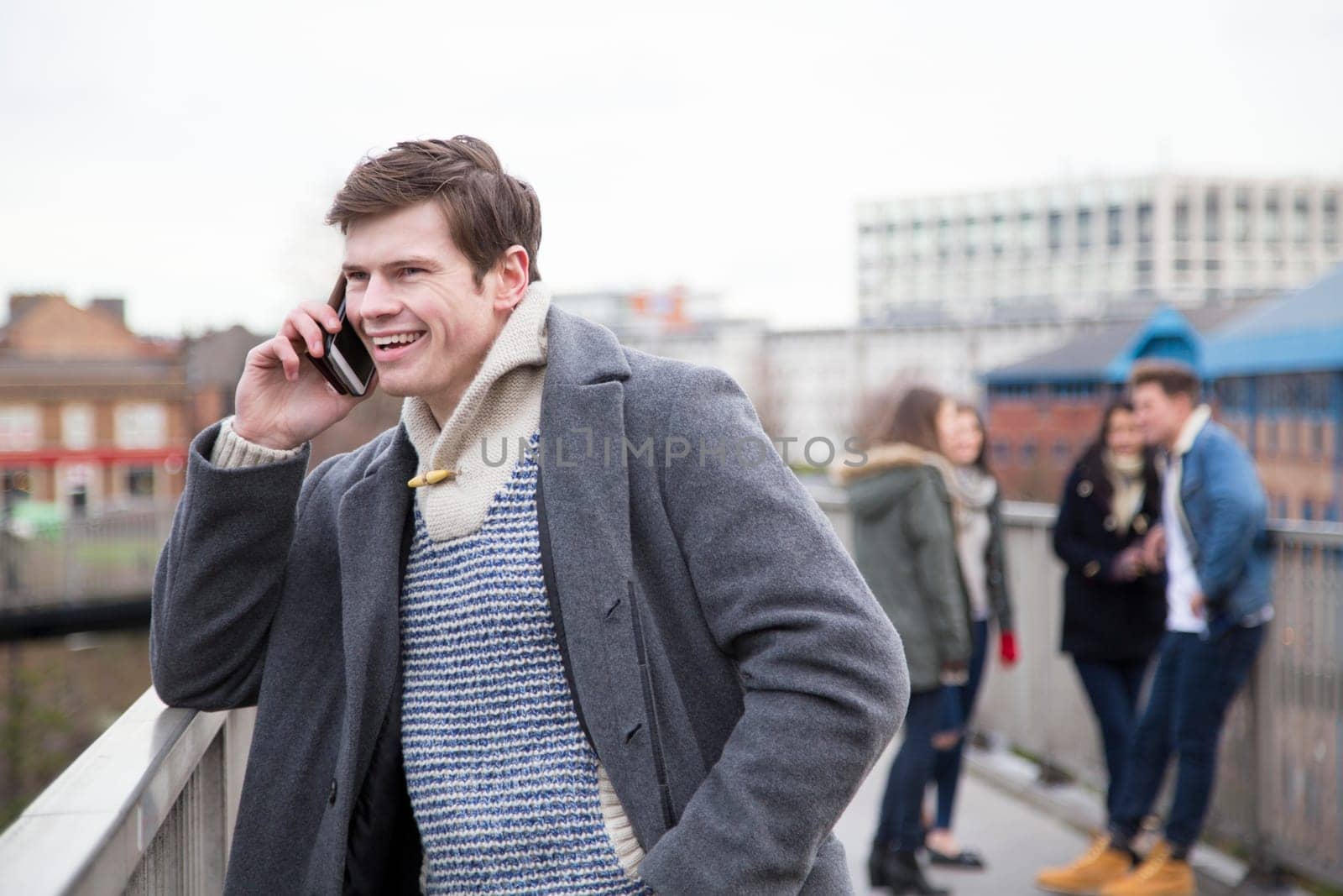 Young adult using a smartphone in the city. A group of people can be seen talking in the background.