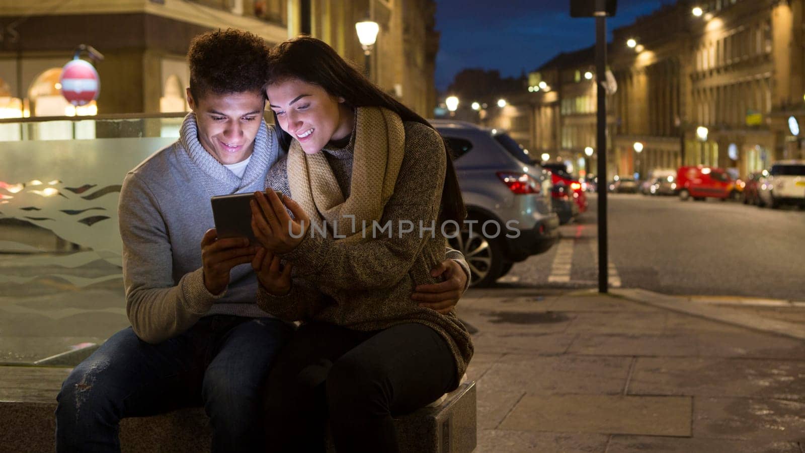 Young couple looking at a digital tablet together. They are sitting in the city at evening.