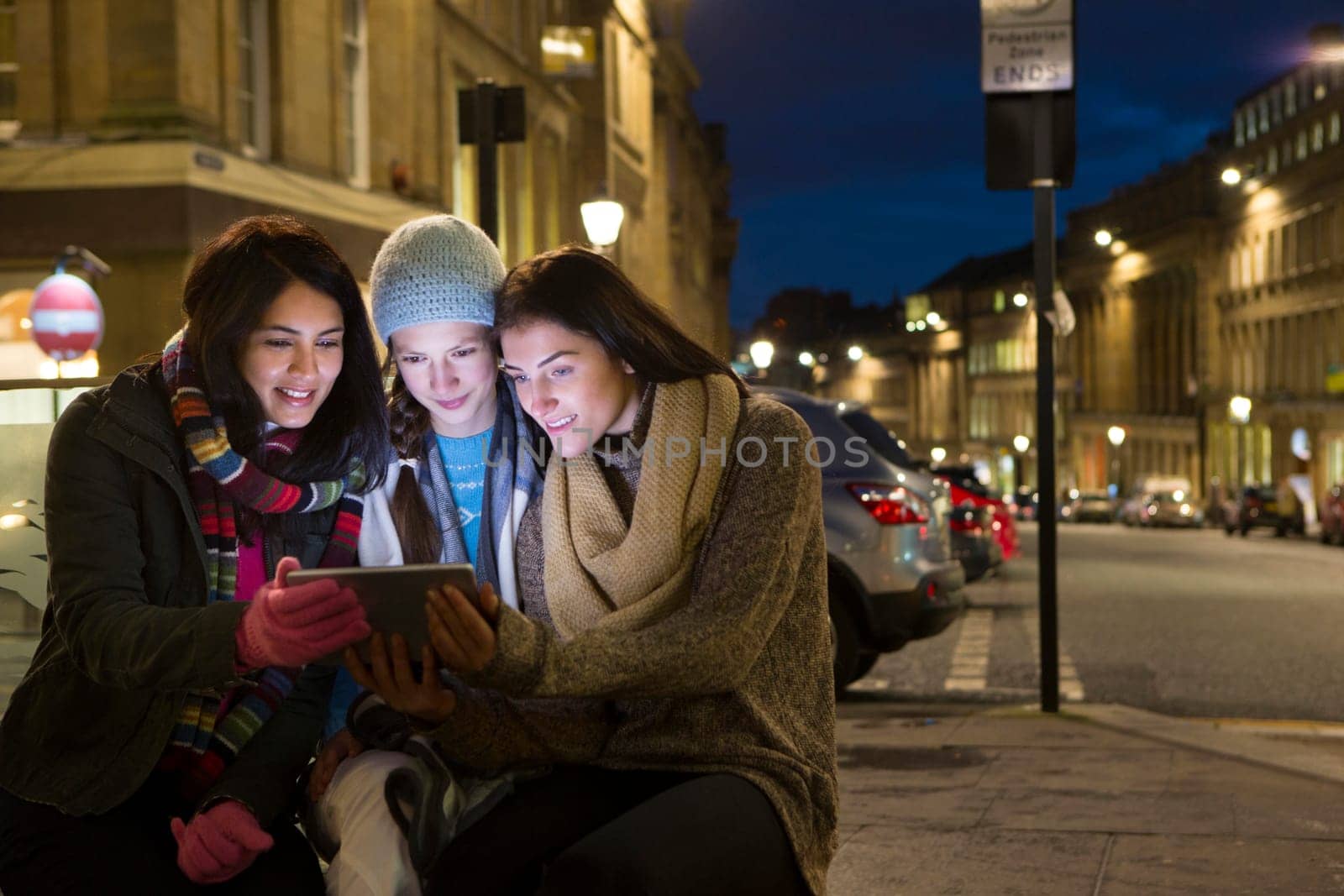Three friends sitting in the city looking at a digital tablet at evening.
