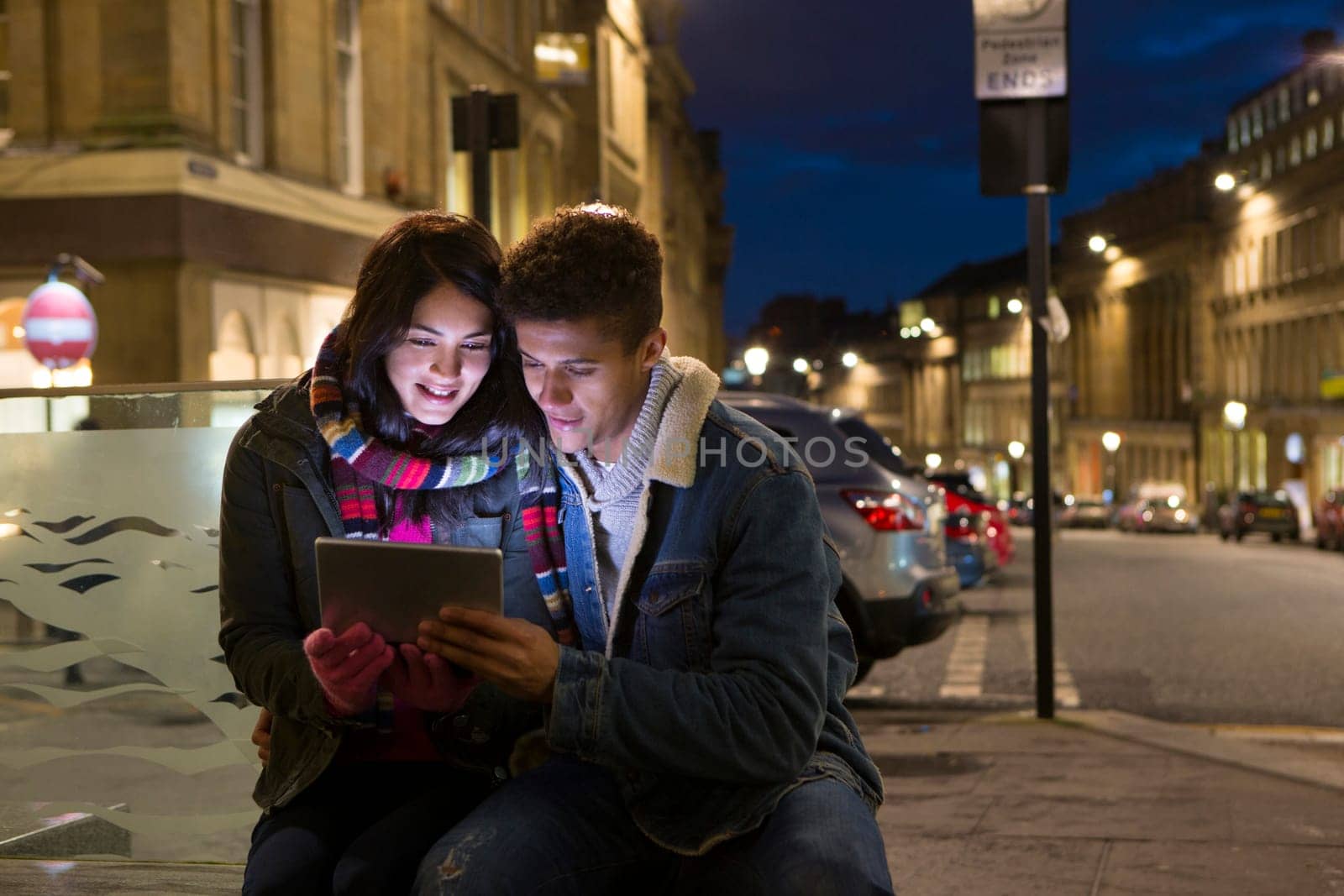 Young couple looking at a digital tablet together. They are sitting in the city at evening.
