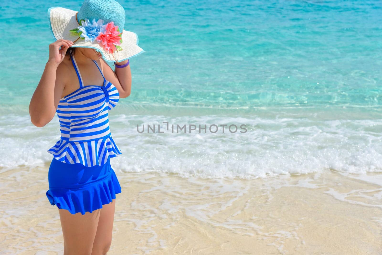 Tourist girl in a blue white striped swimsuit standing with happiness on the beautiful beach and sea during summer at Koh Miang Island, Mu Ko Similan National Park, Phang Nga province, Thailand