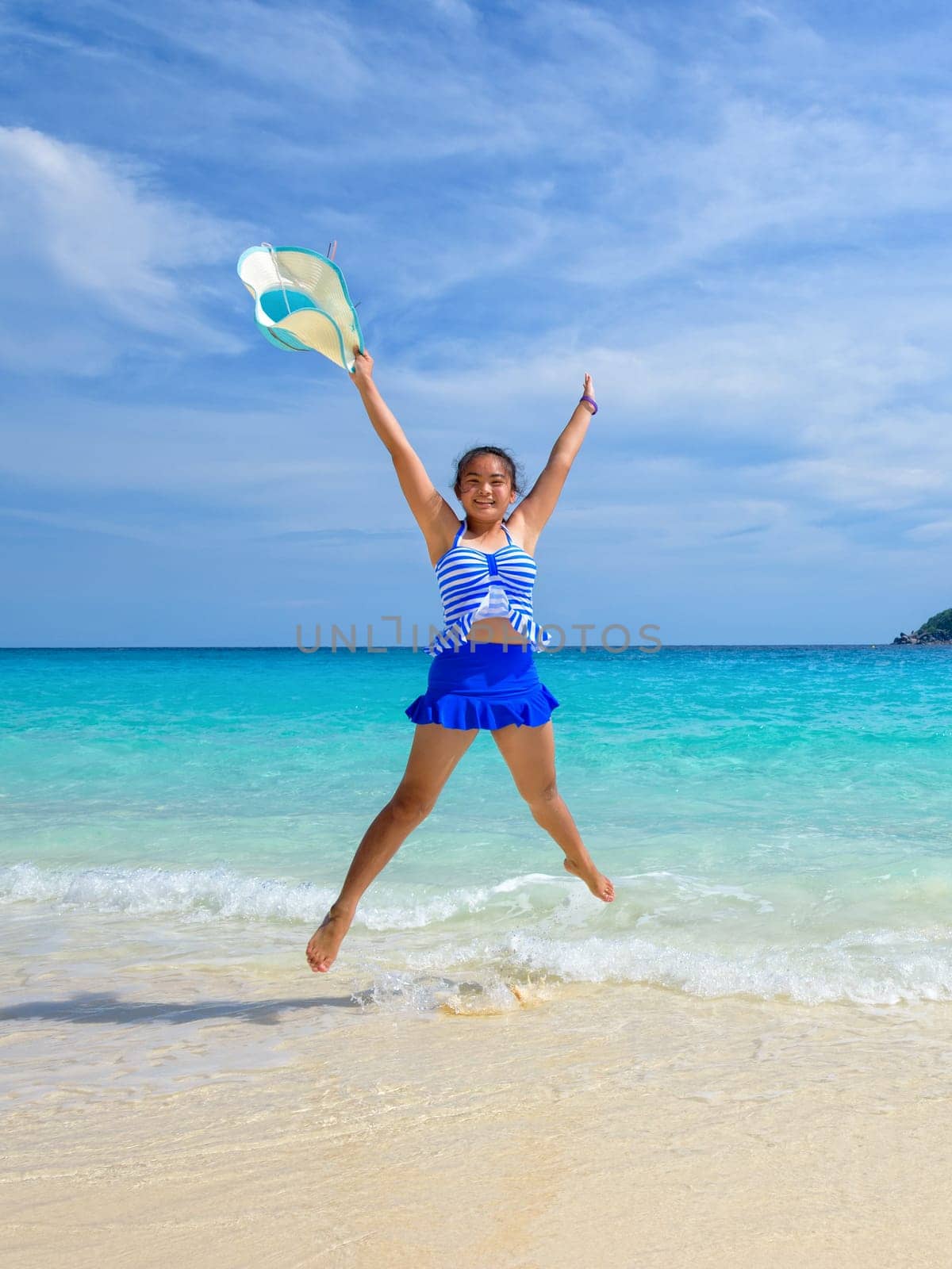Tourist girl in a blue white striped swimsuit jumping shaped X with happy on the beautiful beach and sea during summer at Koh Miang Island, Mu Ko Similan National Park, Phang Nga province, Thailand
