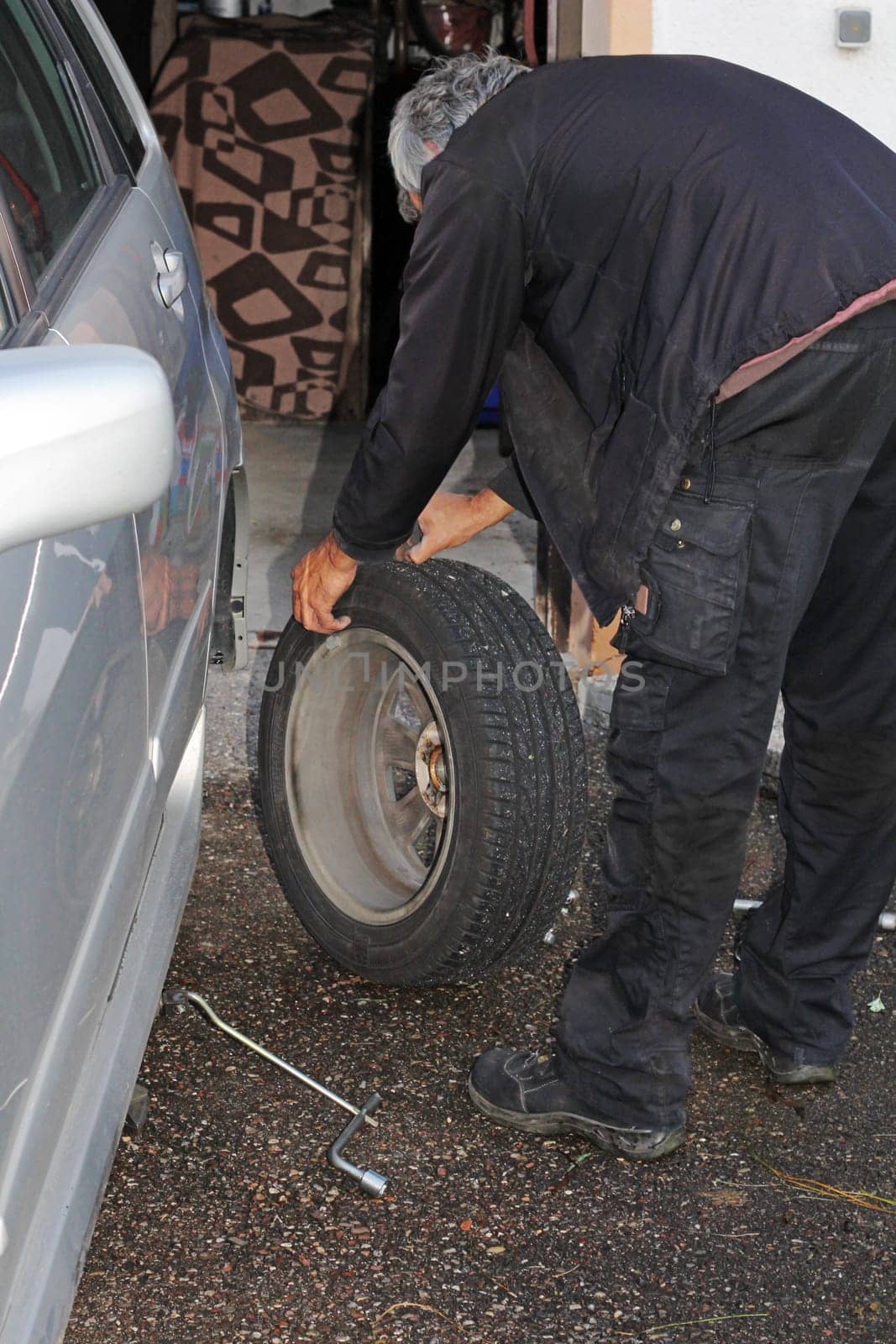 A man mounts winter tires on his car. A man changes the tyres on his car