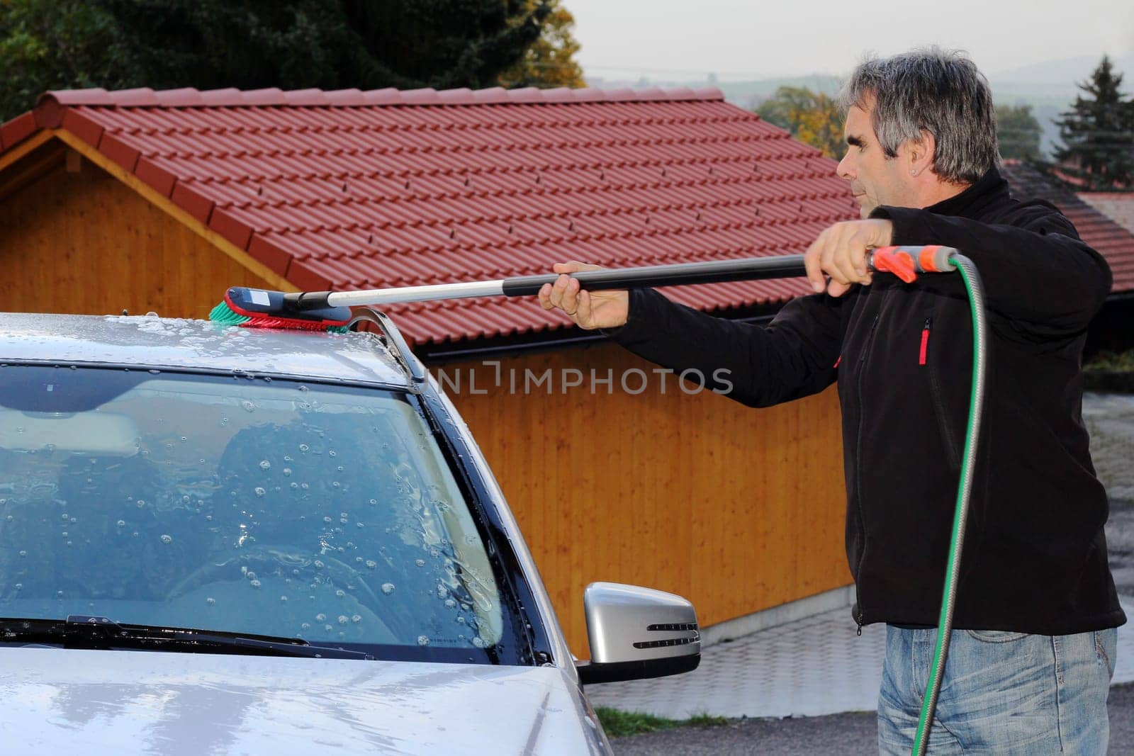A man washes his car with water and a car wash