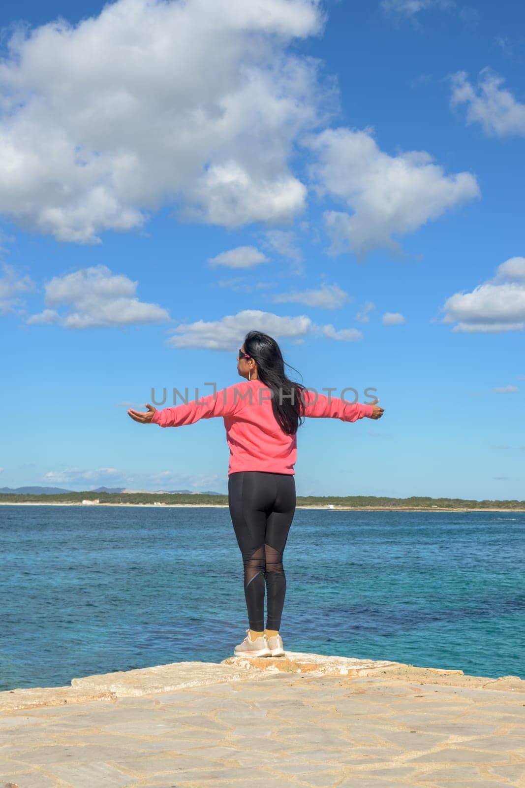 A latin woman stands with her arms open wide, facing the ocean and enjoying the serene view, beautiful latina woman by the sea in Colonia San Jordi, Balearic Islands, Majorca, Spain