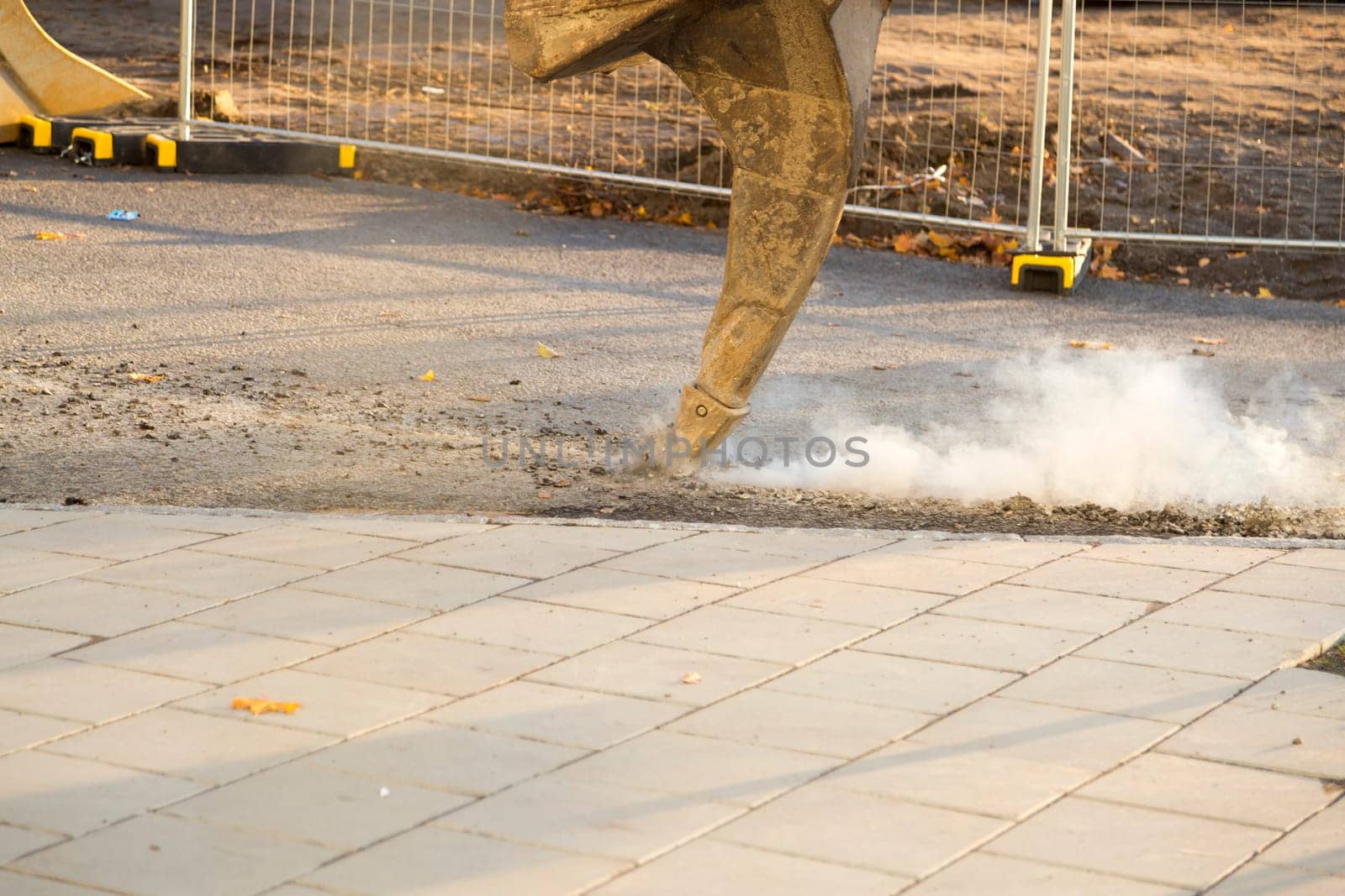 Excavator Ripping Asphalt with fence behind it.