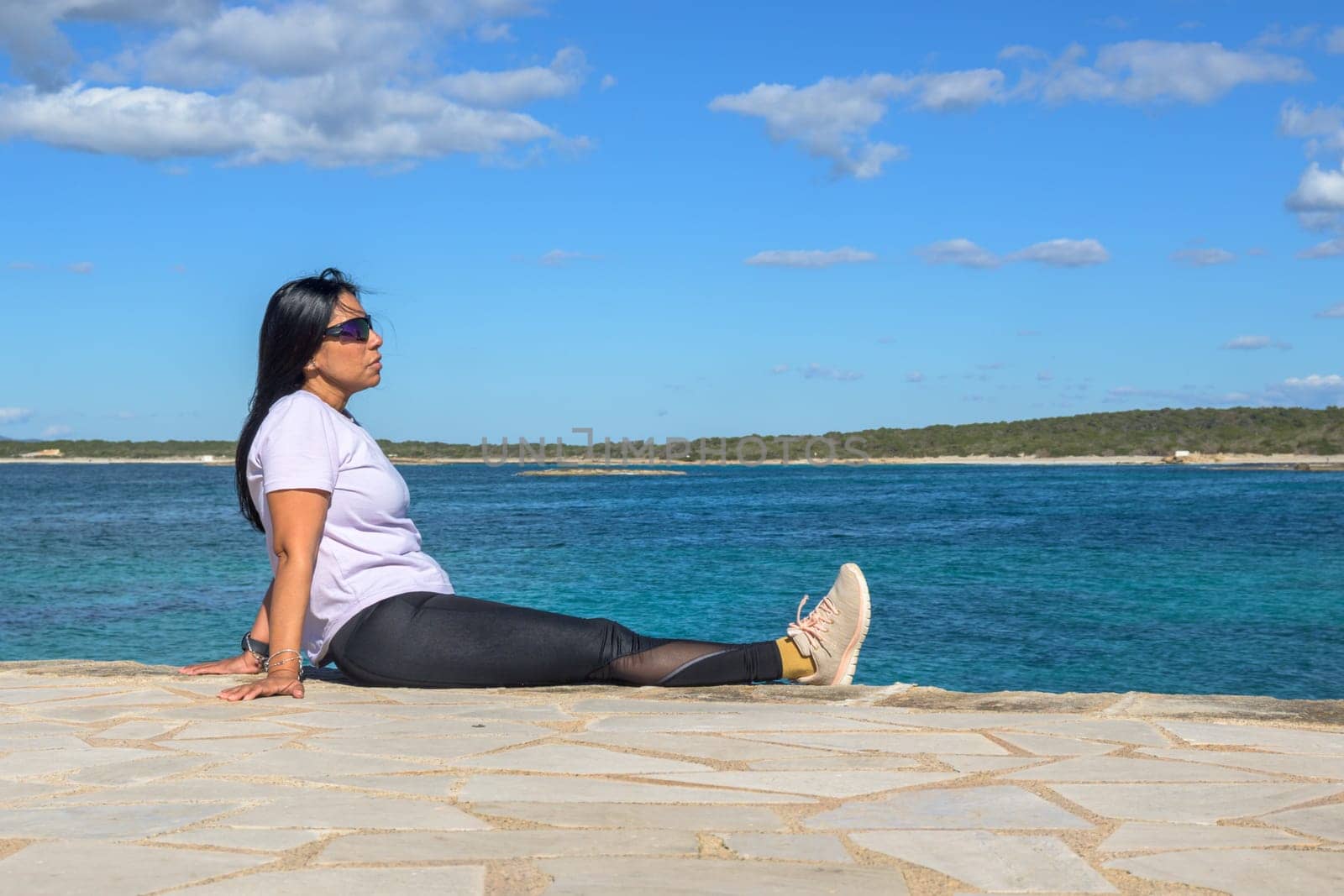 Woman sitting by the ocean, wearing sunglasses, beautiful latina woman by the sea in Colonia San Jordi, Balearic Islands, Majorca, Spain,
