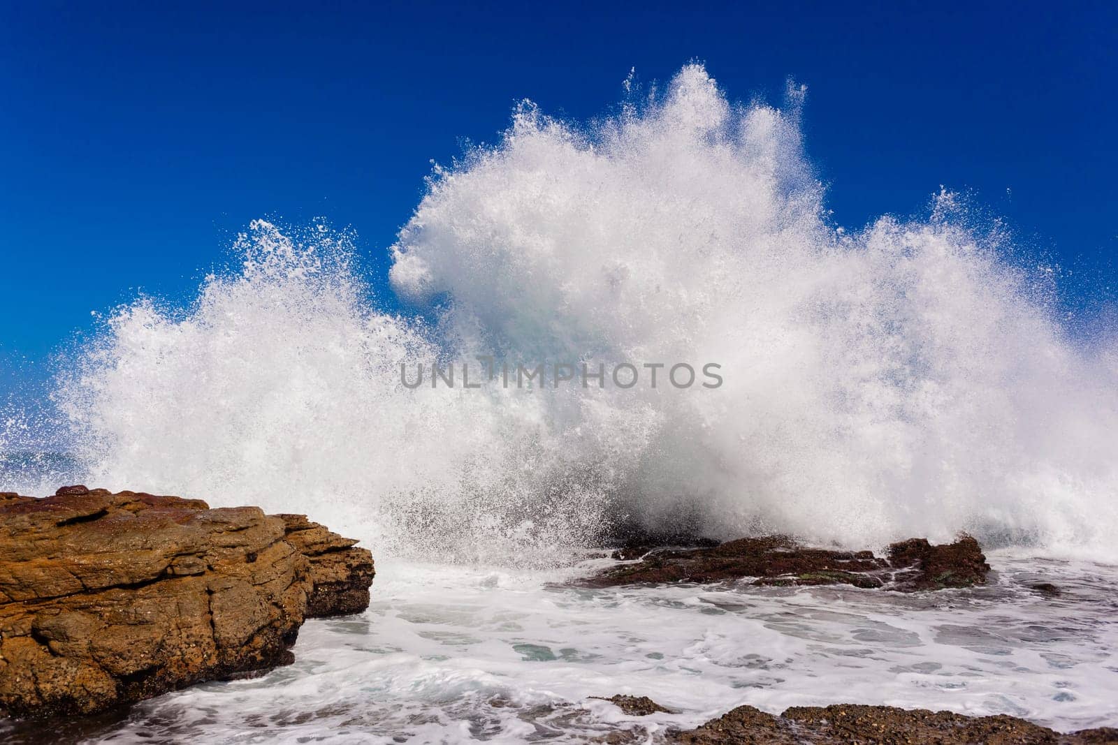 Ocean wave crashing exploding along rocky shoreline exploding white water power