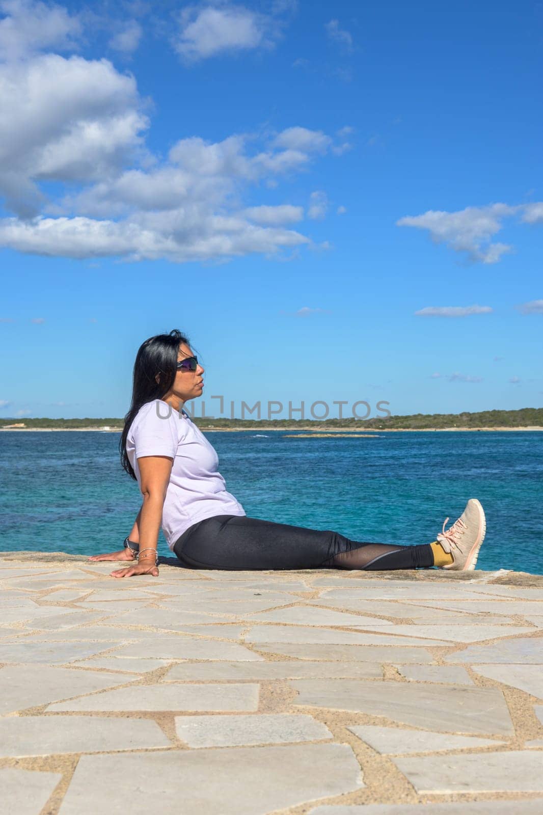 Latina woman, 48 years old, sitting on a pier in Colonia de Sant Jordi, Mallorca, Spain. A sunny early spring day by the turquoise sea, enjoying the peaceful coastal view.